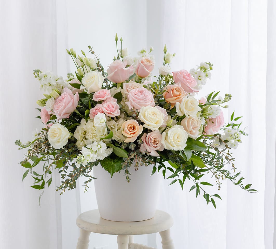 Blush Collection - Luxe  - Soft shades of pink, peach, and ivory—reminiscent of a vintage English garden—come together in our Blush Collection. This arrangement features peach &quot;Shimmer&quot; garden roses, soft pink roses, white Lisianthus, and crisp white hydrangea, accented with Italian Ruscus and Eucalyptus greenery.  Our Luxe sized designs are our most majestic and grand arrangements guaranteed to impress with its volume of blooms, rich design and gorgeous large ceramic vessel (white or gray.) Weight is approximately 30 pounds. Vase makes a lovely planter or vase for years to come.   Product Details: Arrangement is 24&quot; high and 20&quot; wide. Premium size includes an additional 20 stems of flowers and greenery. 
