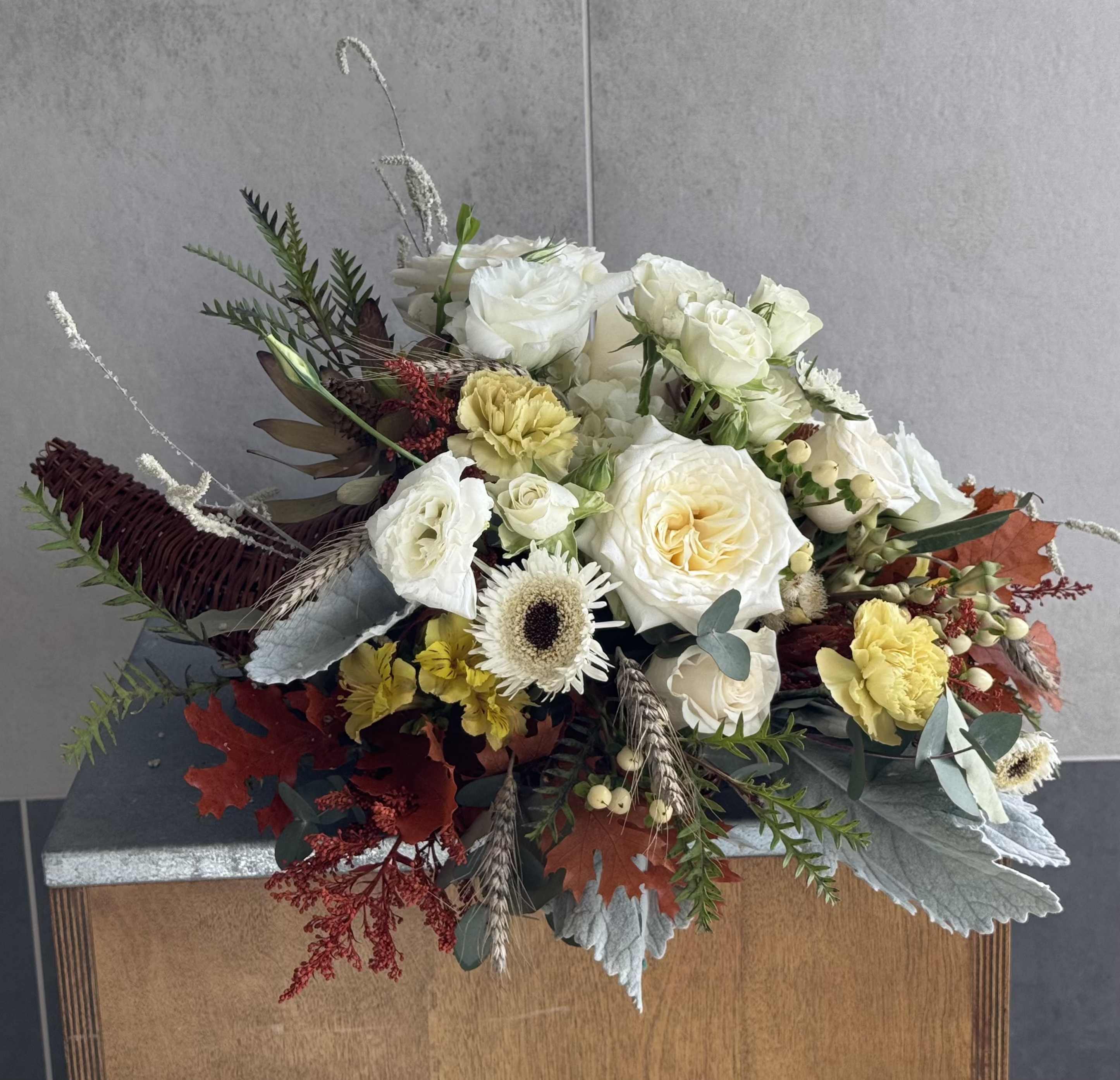 Cream Cornucopia - Bring elegance and warmth to your Thanksgiving table with our Cream Cornucopia. This refined arrangement features soft white roses, delicate spray roses, lush hydrangeas, cheerful mum and charming dry florals, accented by fall leaves in warm, earthy tones. Adding a unique touch, coffee beans are delicately incorporated for a rustic and aromatic flourish.  Housed in a traditional cornucopia basket, this arrangement radiates understated sophistication while capturing the essence of autumn’s beauty. Perfect as a centerpiece or a thoughtful seasonal gift, the Cream Cornucopia is designed to bring grace and gratitude to your celebrations. 