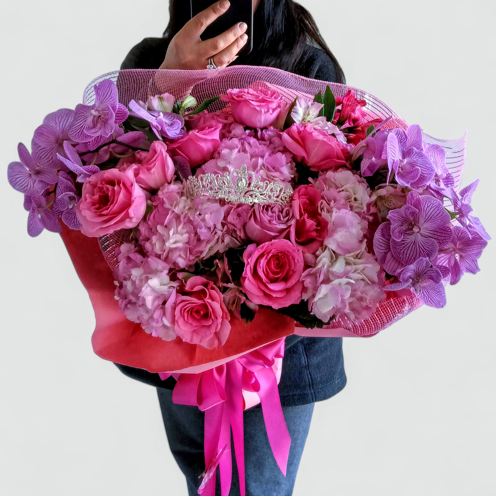The Beautiful One Pink Bouquet - Send this beautiful all pink and lavender blossoms bouquet filled with roses hydrangeas and orchids adorned with a beautiful rhinestone tiara that she can wear and save as a keepsake. Perfect to send for every reason to make their day, wrapped in pretty pink paper and mesh with a long flowing rose pink satin bow with butterflies.