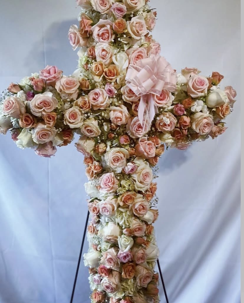 Sacred Rose Remembrance Cross - A timeless symbol of faith, love, and remembrance, this exquisite standing cross is handcrafted with hundreds of premium garden-style roses in soft blush, peach, and cream tones. Designed with lush fullness and meticulous attention to detail, each bloom is placed to create a seamless tapestry of beauty and comfort.  Accented with delicate filler florals and finished with an elegant satin bow, this piece brings a sense of peace and reverence to any memorial service, celebration of life, or religious ceremony. Standing tall on a secure easel, it offers a heartfelt tribute that speaks when words fall short.  Custom color palettes are available upon request to honor your loved one with a personalized touch. 