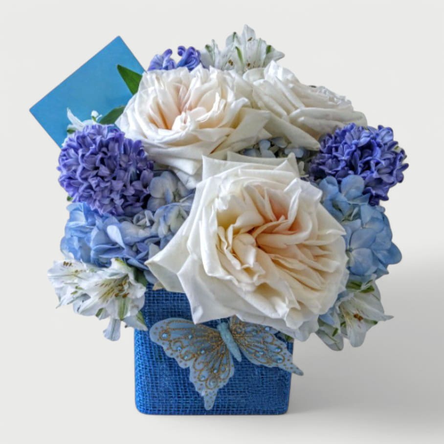 Blue Hydrangea Designer's Choice - Beautiful blue and white roses hydrangeas and more arranged in a pretty modern glass vase wrapped in lovely blue jute ribbon adorned with a sweet spring blue butterfly. Perfect for every reason to show them how much you care. Send happiness.
