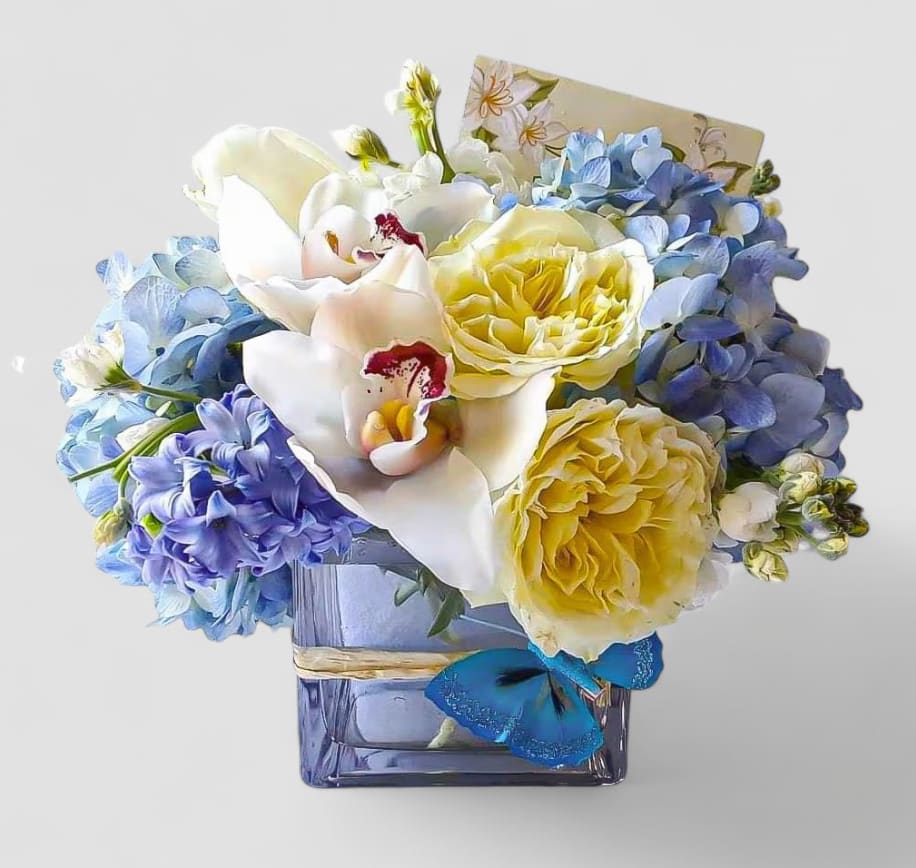 Blueberry And Creme Bouquet Designer's Choice - Send this beautiful bouquet today for every occasion to make them smile with it's lovely mixed blue and vanilla blossoms of the day roses orchids hydrangeas and more arranged in a modern glass cube vase. Always  made extra special and unique each time. Send happiness.