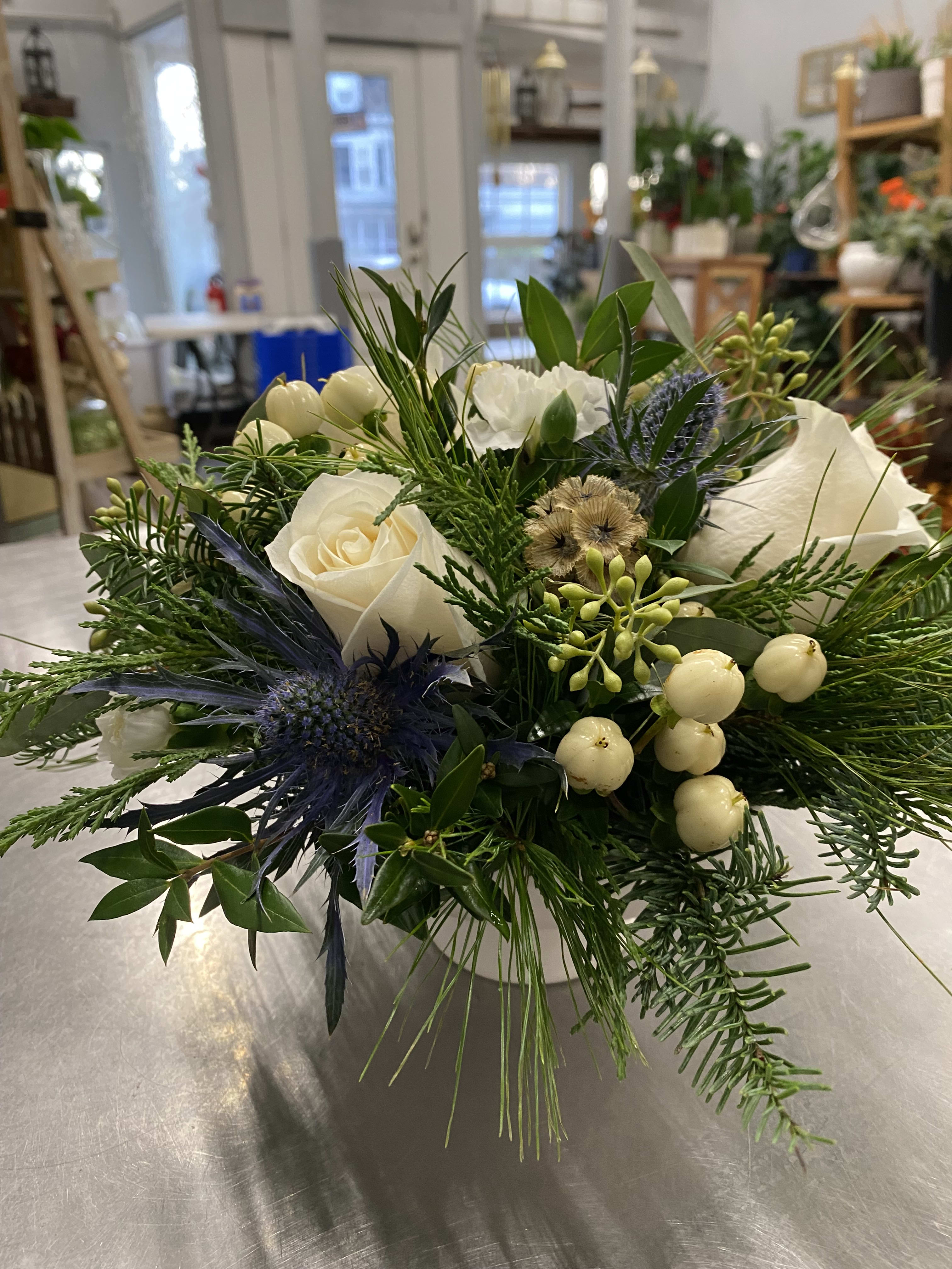 Natural Winter - A elegant design in a ceramic container that will include white roses, hypericum berries, thistle, eucalyptus and fresh beautiful evergreens.