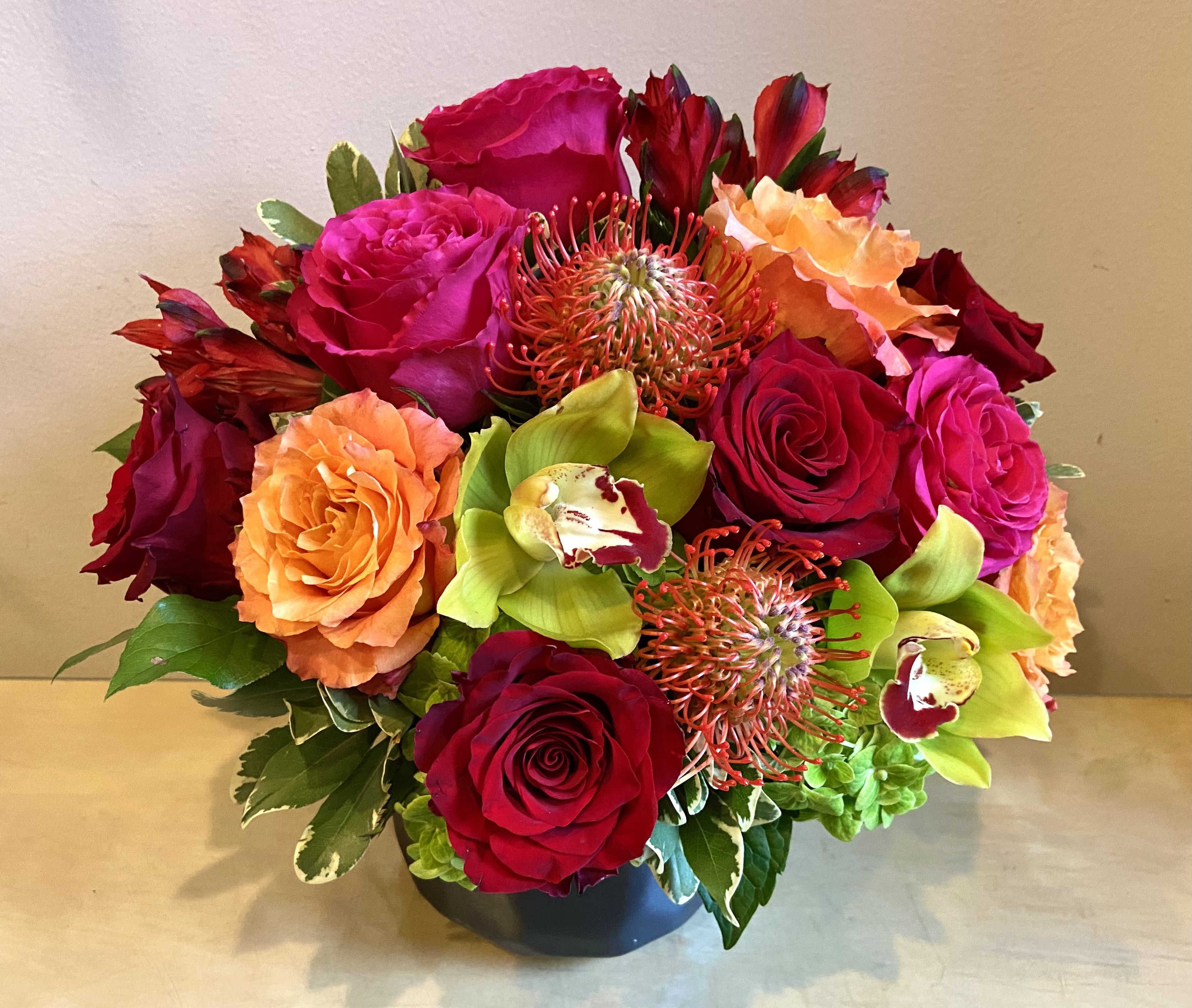 Heart to Heart - Beautiful warm vibrant hues of roses &amp; pin cushion protea against lime green orchids &amp; hydrangea in a clssic black ceramic vase.