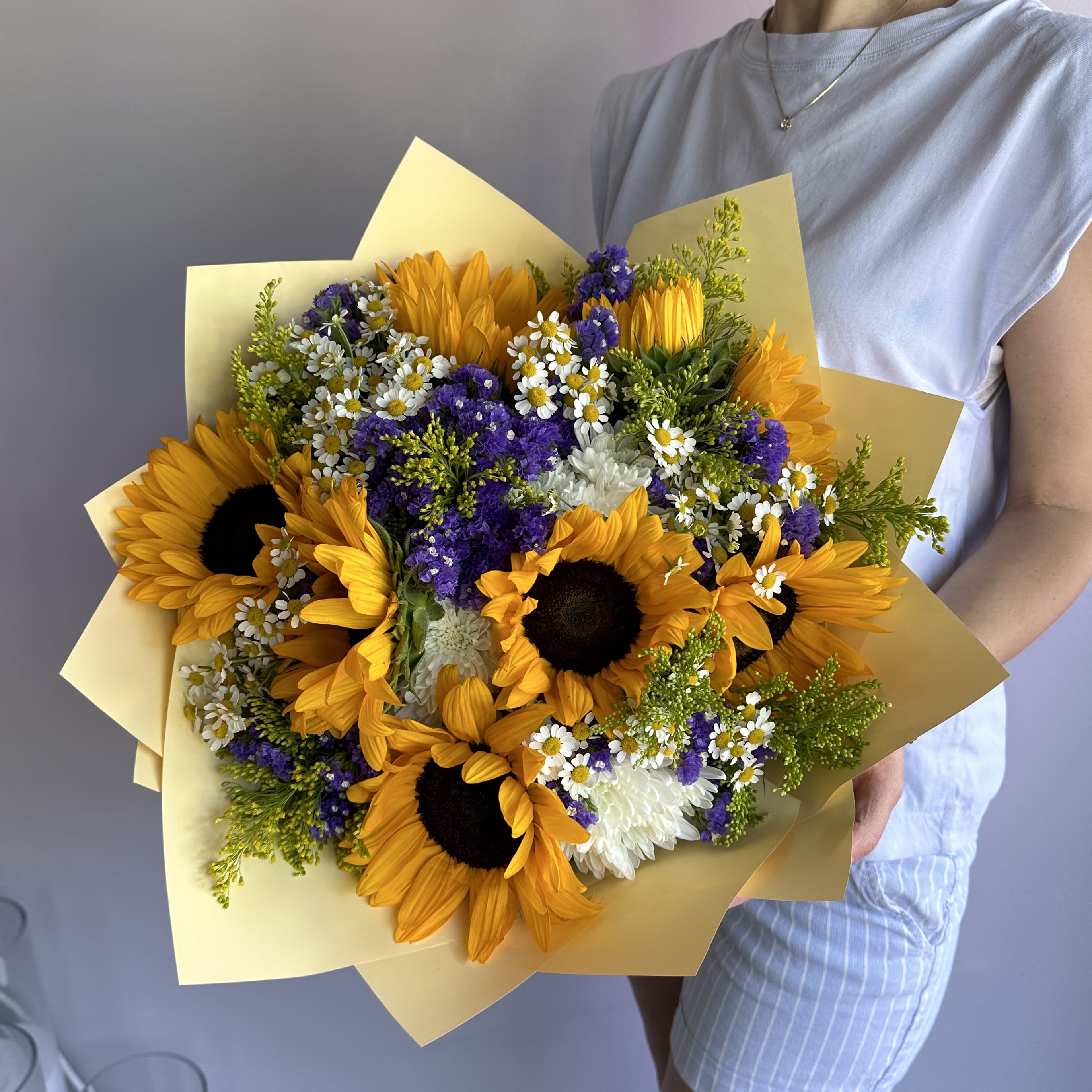 69P- Sunny Bouquet - Bring sunshine into someone's life with this vibrant sunflower bouquet. Bursting with bright yellow sunflowers, delicate white daisies, and rich purple accents, this stunning arrangement is wrapped in soft yellow paper to enhance its cheerful, radiant look. Perfect for birthdays, anniversaries, or any celebration, this fresh sunflower bouquet adds a pop of color and joy to any occasion. The Premium size is shown in the picture.