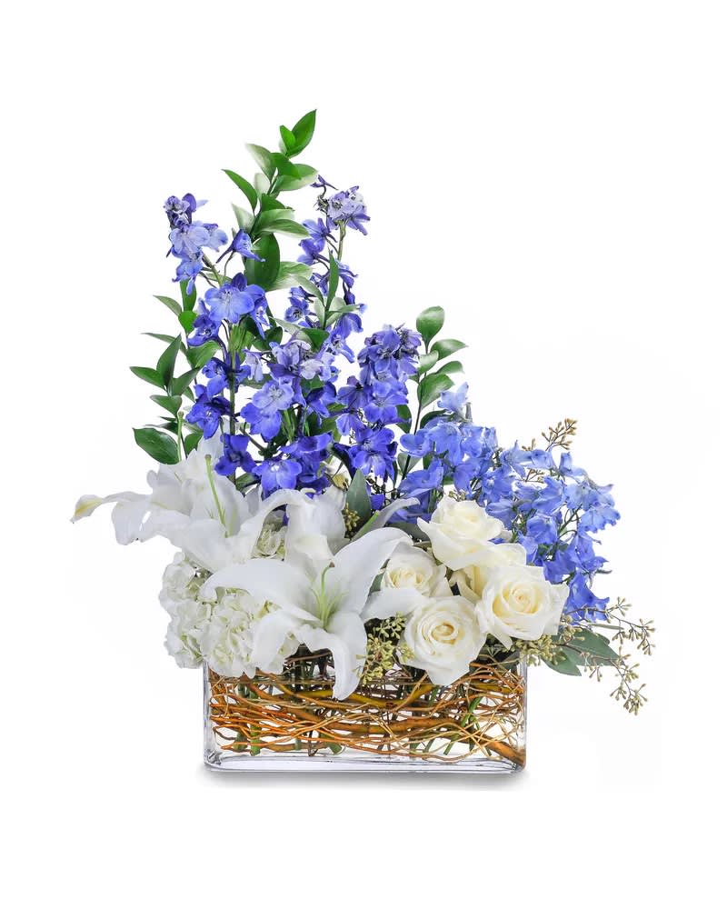 Majestic Blue - This chic bouquet includes striking blue delphinium, elegant white roses, hydrangea and majestic lilies and are designed within the curly willow filled clear glass rectangle vase. A beautifully designed centerpiece of white roses, hydrangea and shades of blue delphinium accented with seeded eucalyptus.