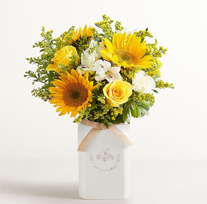 Honey Bee Buzz For Summer - Get them buzzing for summer! Our unique bouquet is gathered with a mix of blooms in bright, happy yellow and white. Designed in our Sweet As Can Bee artisanal vase, featuring an adorable honeybee and a raffia bow, it’s a gift that adds radiant beauty to any decor.