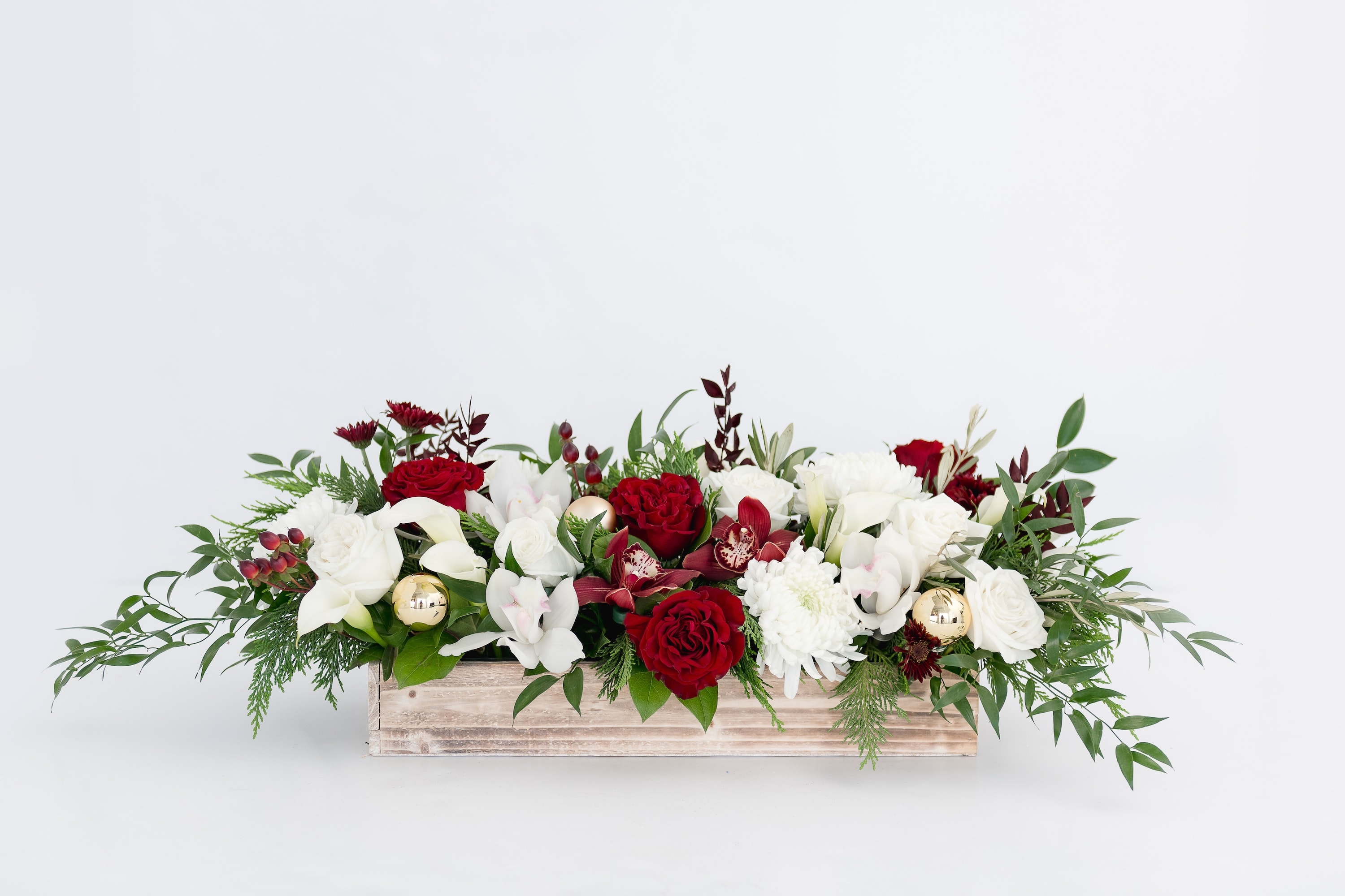 Joyful Collection Grand Centerpiece  - A gorgeous, full arrangement in deep reds and classic white in a white-washed wood box. A bed of Cedar, Olive branch and Italian Ruscus layered with red &quot;Hearts&quot; garden roses, white garden roses, burgundy spray mums, berries, white and red Cymbidium orchid florets, white Callas lilies, gold ball ornaments, and Olive branch, elegant cedar greens. A true WOW design perfect for a thank you gift or a stunning addition to a holiday table.   Product Details: Arrangement is approximately 20&quot; wide and 8&quot; deep. Container is a wood box with liner. 