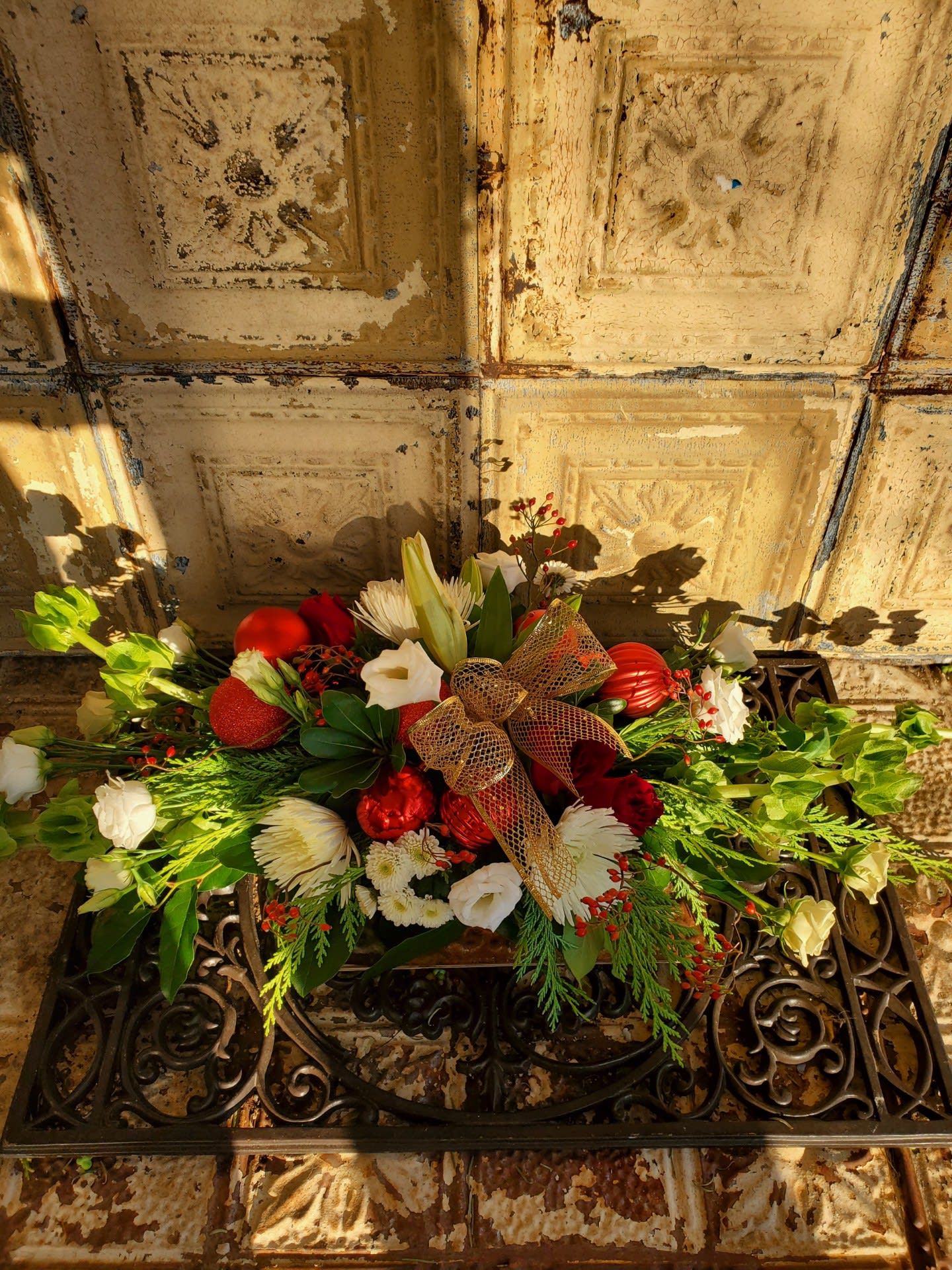 Marie Curie - This centerpiece made of roses and spray roses, lilies, mums, button poms, lisianthus, rose hips, cedar, pittosporum, bells of Ireland, Christmas ornaments, and decorative ribbon. 