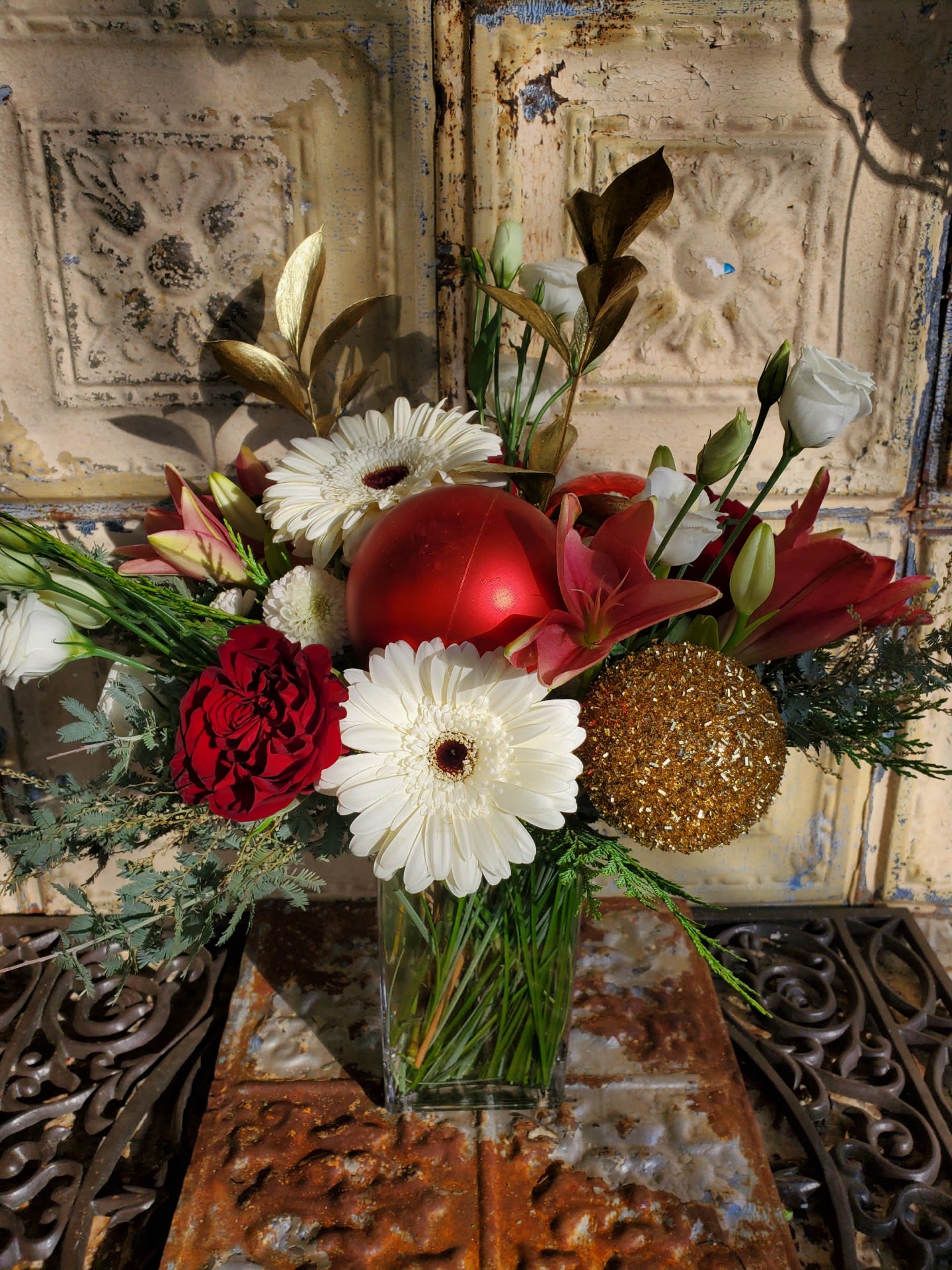 Queen Victoria - A stunning Christmas arrangement with gerbera daisies, acacia, lilies, roses, lisianthus, button poms, cedar, gold gilded Israeli ruscus, and assorted Christmas ornaments.