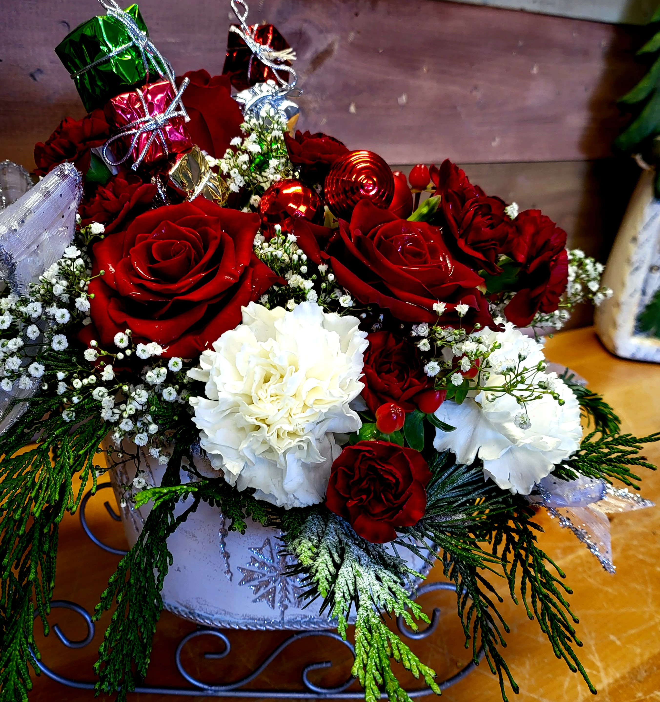 Christmas Sleigh Arrangement - Let Santa come in on a sleigh to your home this season. Container will vary from picture. Flowers can vary due to season and availability, that includes the greens that are pictured. Mixed Bouquets