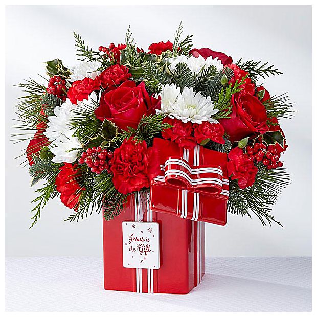 FTD Jesus Is The Gift - The true gift of the season is the gift of the life Jesus. In celebration of this holiday honoring His birth, the DaySpring® Jesus is the Gift™ Bouquet is a perfectly merry way to honor this treasured time with friends and family. FTD® has partnered with DaySpring® to create this unique collection that helps you &quot;Live Your Faith&quot; in all life's moments, great and small. Arranged by an FTD® floral artisan, this bouquet brings together red roses, red carnations and mini carnations, white chrysanthemums, variegated holly, and Christmas greens. Presented in a keepsake red ceramic vase mimicking the look of a holiday package, with the sentiment, &quot;Jesus is the Gift,&quot; lettered at the center, and arriving with a lid for future use for many Christmas celebrations to come, this holiday bouquet is a stunning way to send your warmest holiday greetings this season. GOOD is approx. 11&quot;H x 12&quot;W