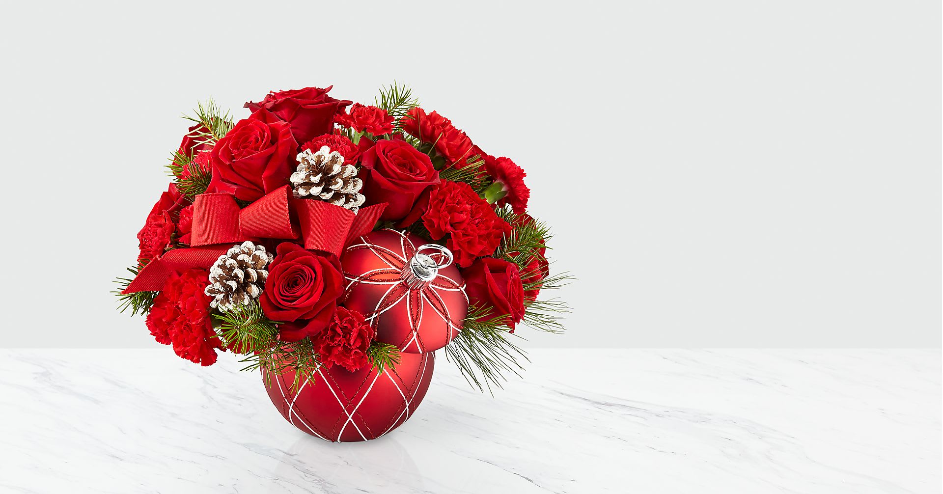 Making Spirits Bright - Deck the halls, and their holiday home with a bouquet that shares the most beautiful season's greetings. Bright red roses, red carnations and Christmas greens come together within an ornament vase with stem lid to create our Making Spirits Bright Bouquet. Featuring a bold red ribbon and natural pinecone pics, this arrangement captures the joy of holiday magic for whoever it's given to.