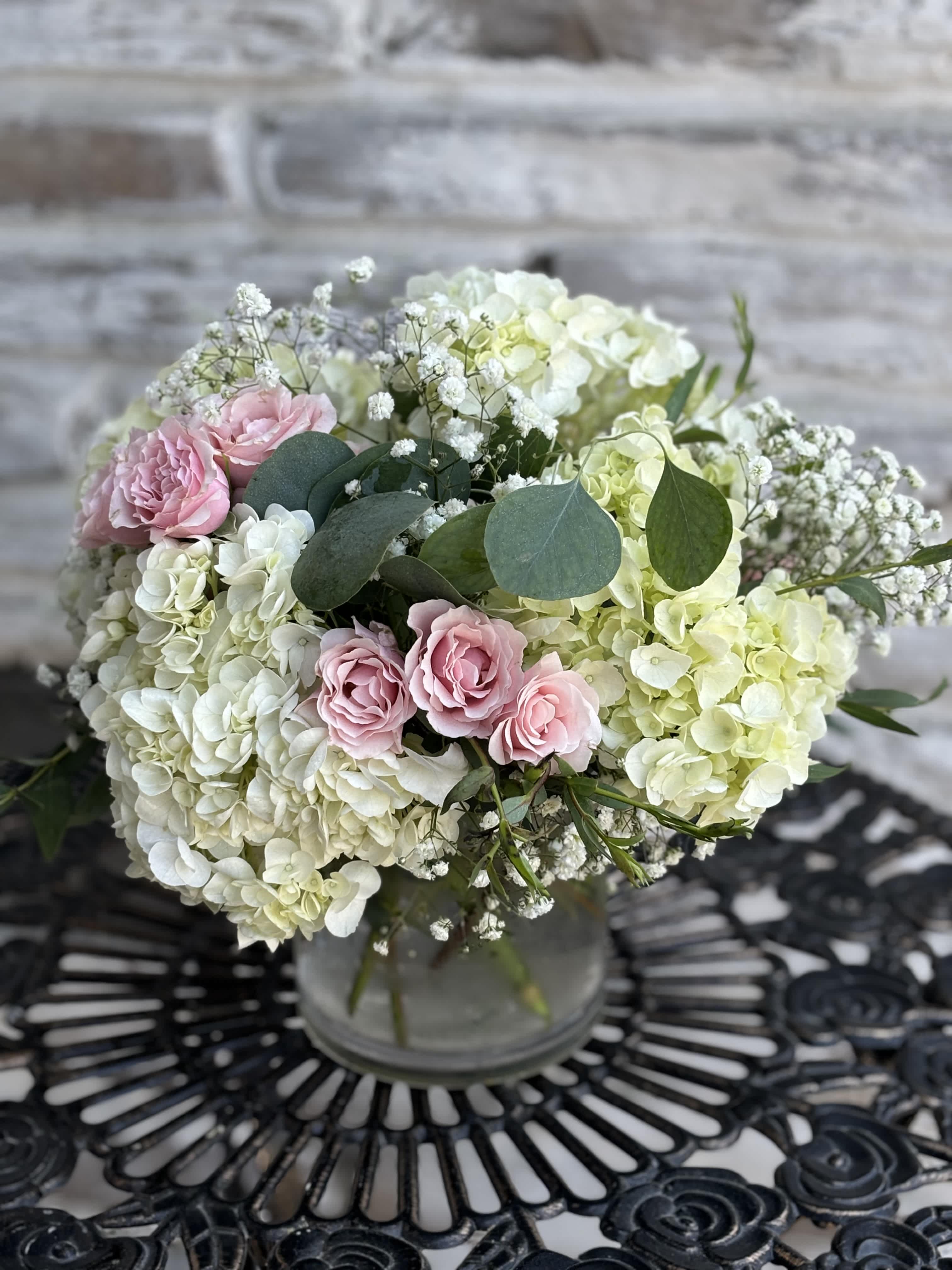 Emily Baby Pink  - White hydrangeas, Pink spray roses, baby's breath and mixed eucalyptus foliage. Designed all around in a 5x5 cylinder vase.    