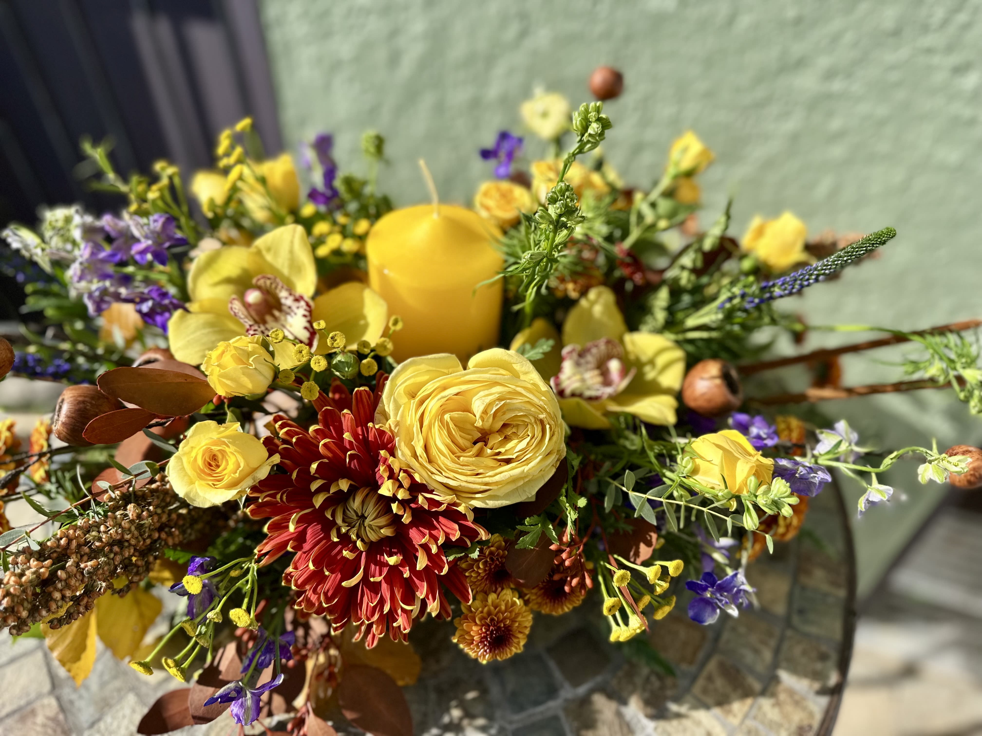 Golden - Embrace the abundant spirit of the season with our radiant &quot;Golden&quot; centerpiece. This exquisite arrangement blends the warmth of sun-kissed yellow roses and elegant orchids with the rich, earthy tones of red and orange chrysanthemums and natural dried accents. A glowing central candle casts a cozy light, transforming any gathering into a truly warm and inviting occasion. Perfect for your Thanksgiving table, this design captures the essence of the autumn harvest and is sure to be a stunning focal point and a wonderful conversation starter for your guests. Celebrate gratitude with the timeless charm and rich colors of fall!