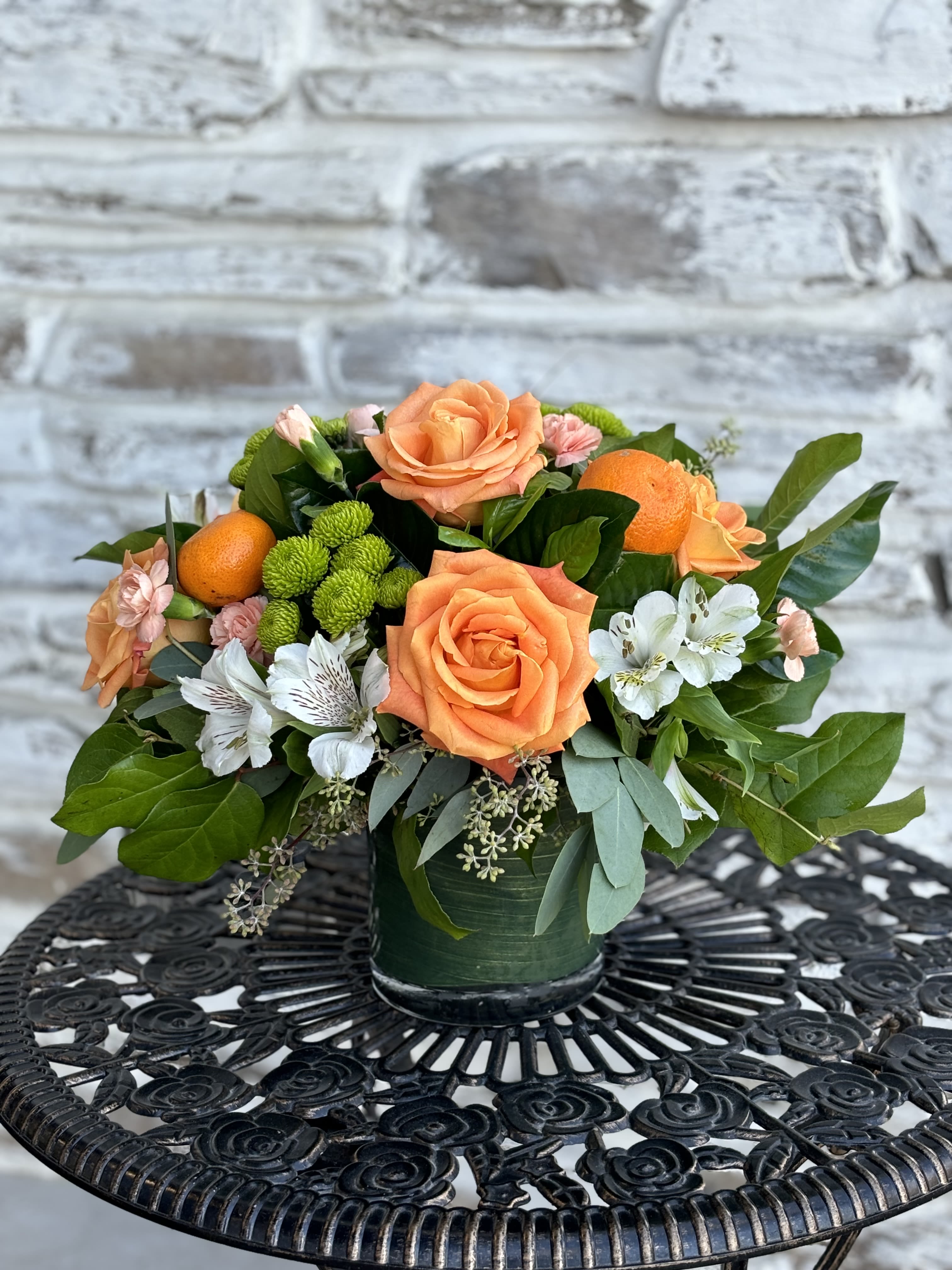 What A Cutie - This cute citrus arrangement will leave you feeling refreshed and full of joy.  Cylinder vase filled with orange coral roses and verdant greens with a pop of white blooms fill this arrangement with beauty and light. This arrangement is perfect for a birthday, housewarming, or anniversary gift. 