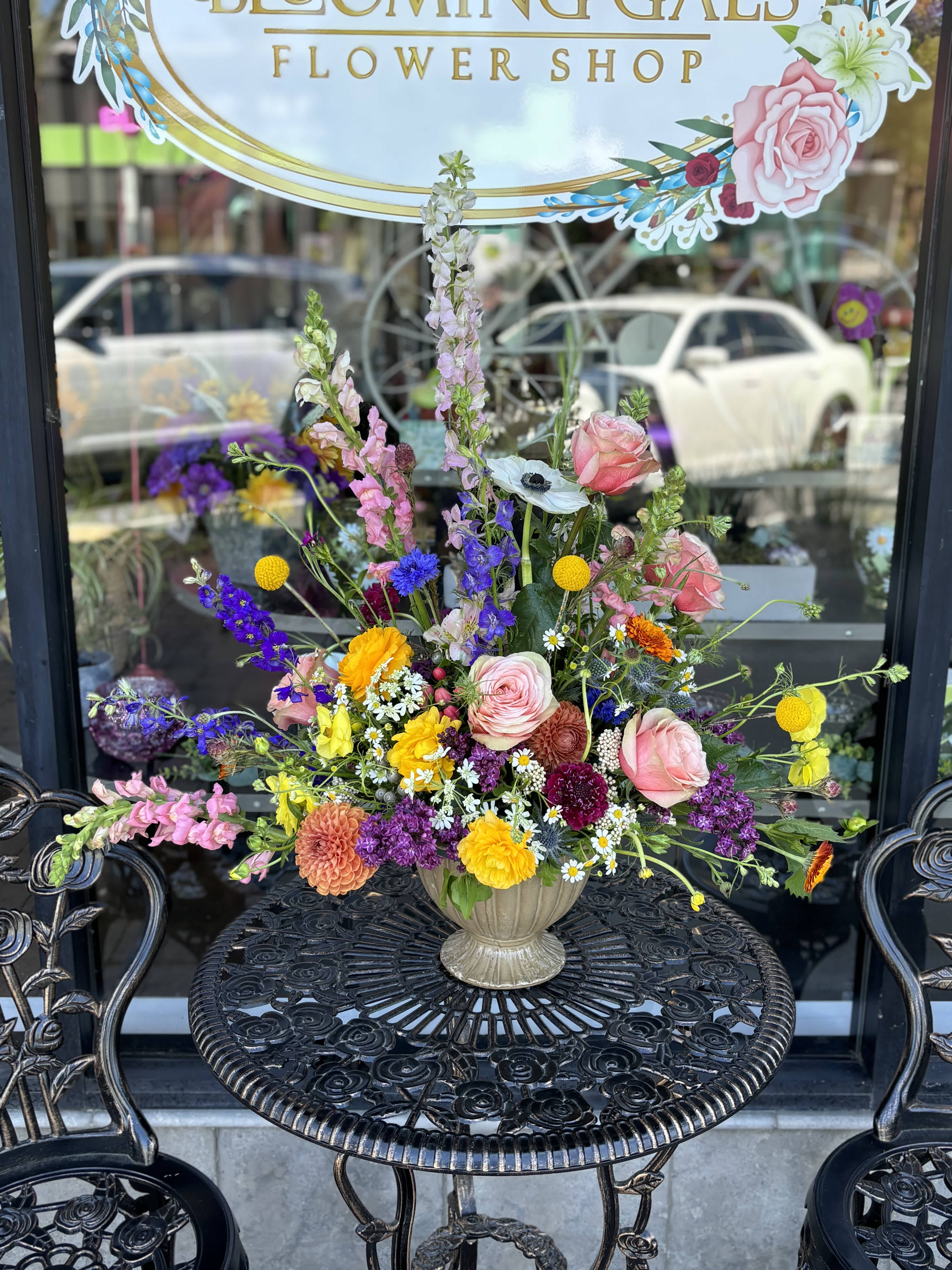 Flowers in the Prairie - Mixture of wildflowers with a touch of roses, ranunculus, dahlias and larkspur arranged in a pedestal vessel. All around arrangement. 