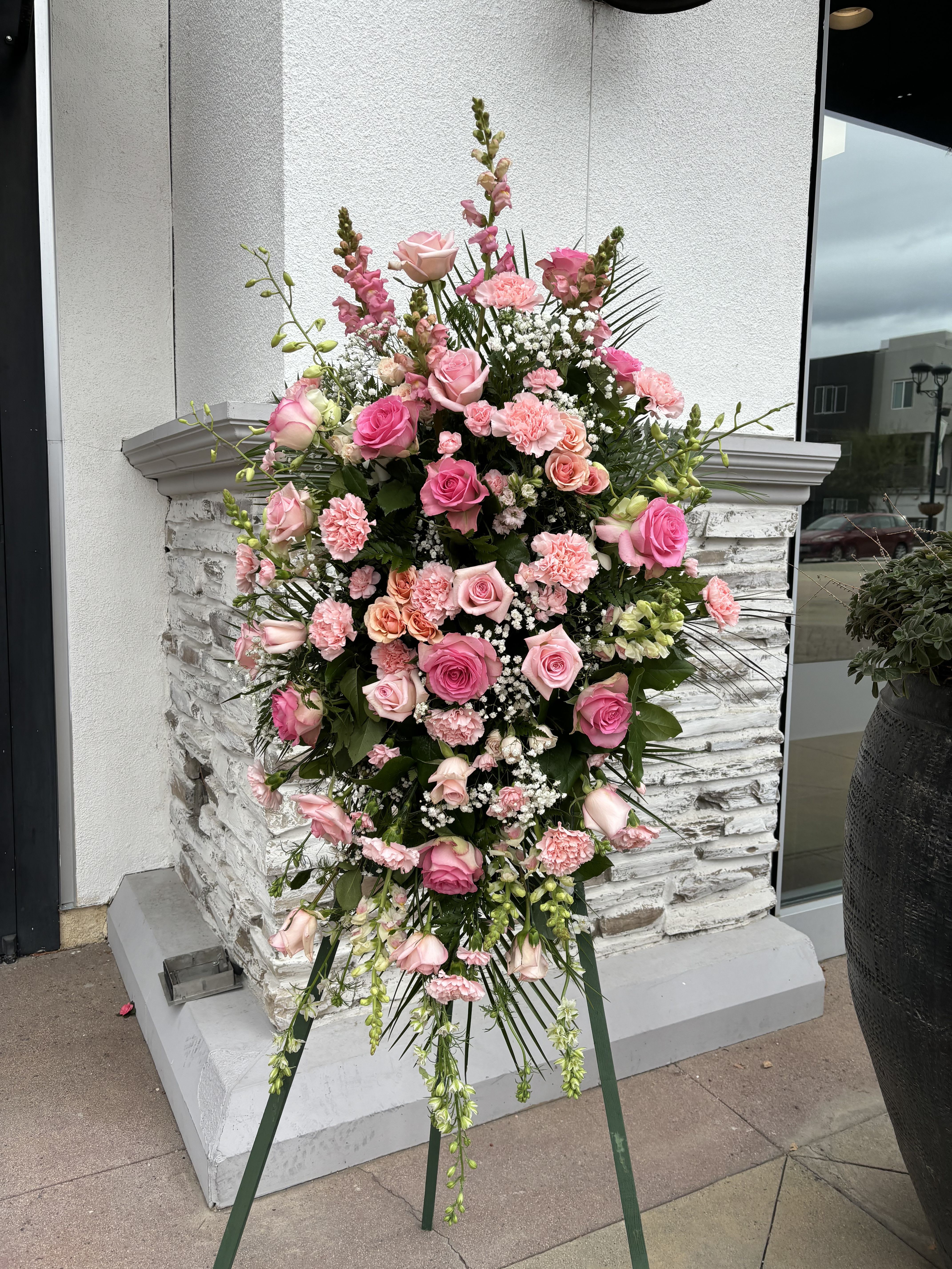 Peaceful Pink Standing Spray -  This feminine standing spray is a pink garden of roses, carnations, snapdragons, larkspur, mini carnations, mini spray roses and baby's breath.  One sided standing spray.
