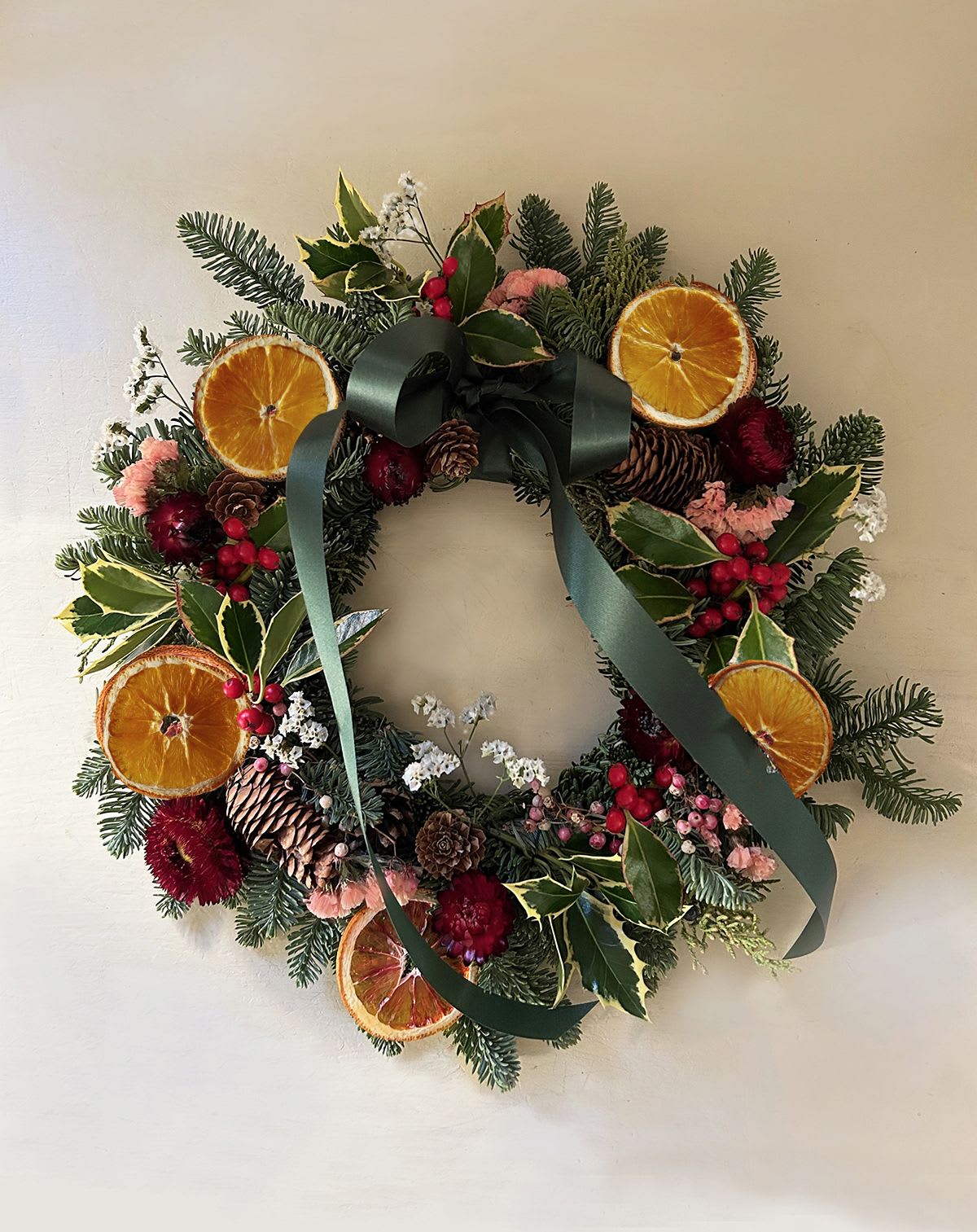Martha Wreath - A beautiful, classic holiday wreath for outdoors and indoors. A base of noble fir decorated with beautiful holly, pine cones, straw flowers, pink peppers, fresh dried orange slices and dried white flowers. Decorated with a moss green bow and hook for hanging. Appx 12&quot;, it is not a large wreath but will fit on regular doors. Ready for hand delivery in LA. To ship the wreath throughout United Stated head to www.blomstlosangeles.com