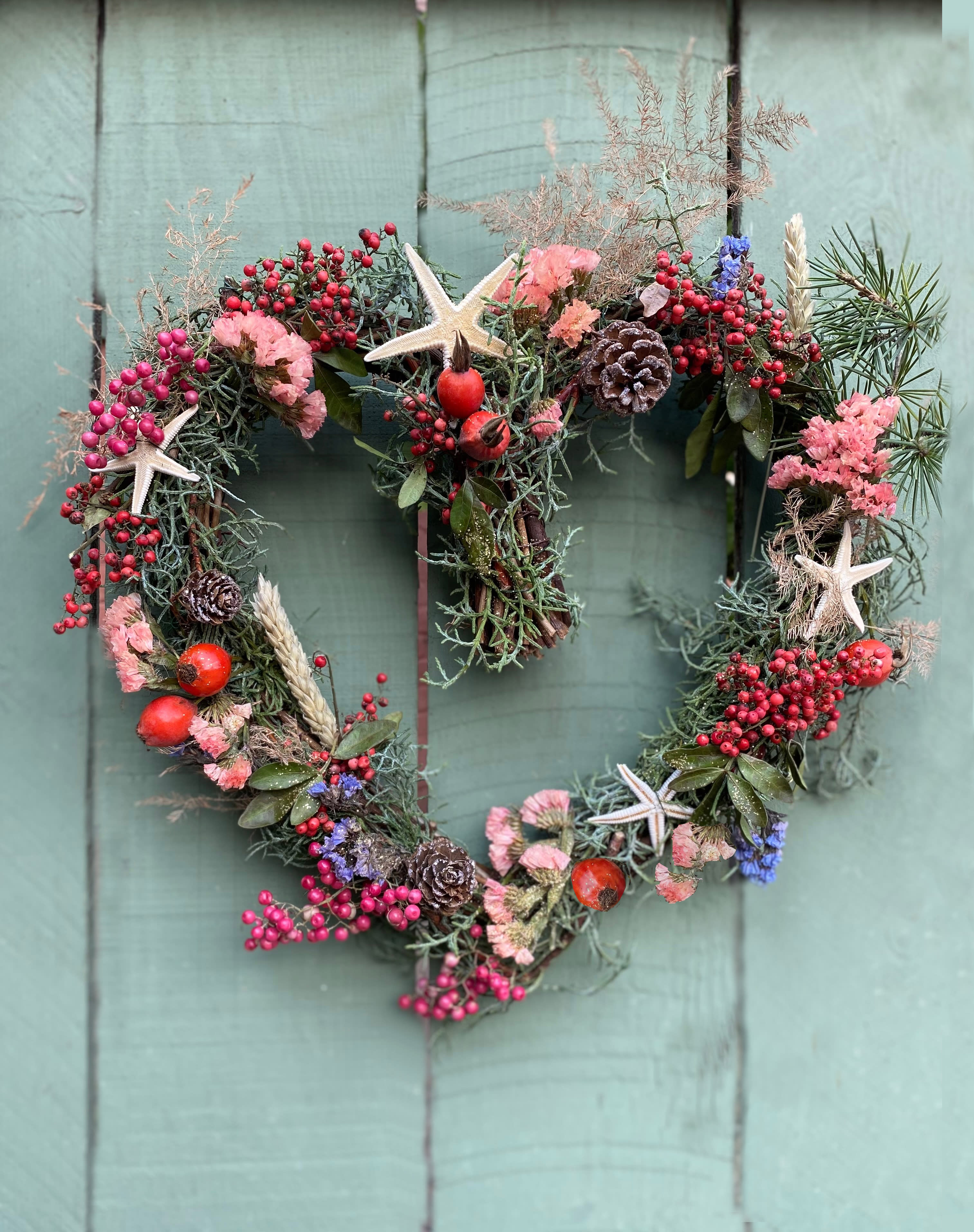 Hermione Heart Wreath - Gorgeous and natural heart shaped wreath, made on a base of vines and decorated with peppers, rose hips or other similar seasonal berries, pines, shells and other natural elements, all in lovely warm colors. The heart is 10&quot; wide, can be hung on door or laid on table.