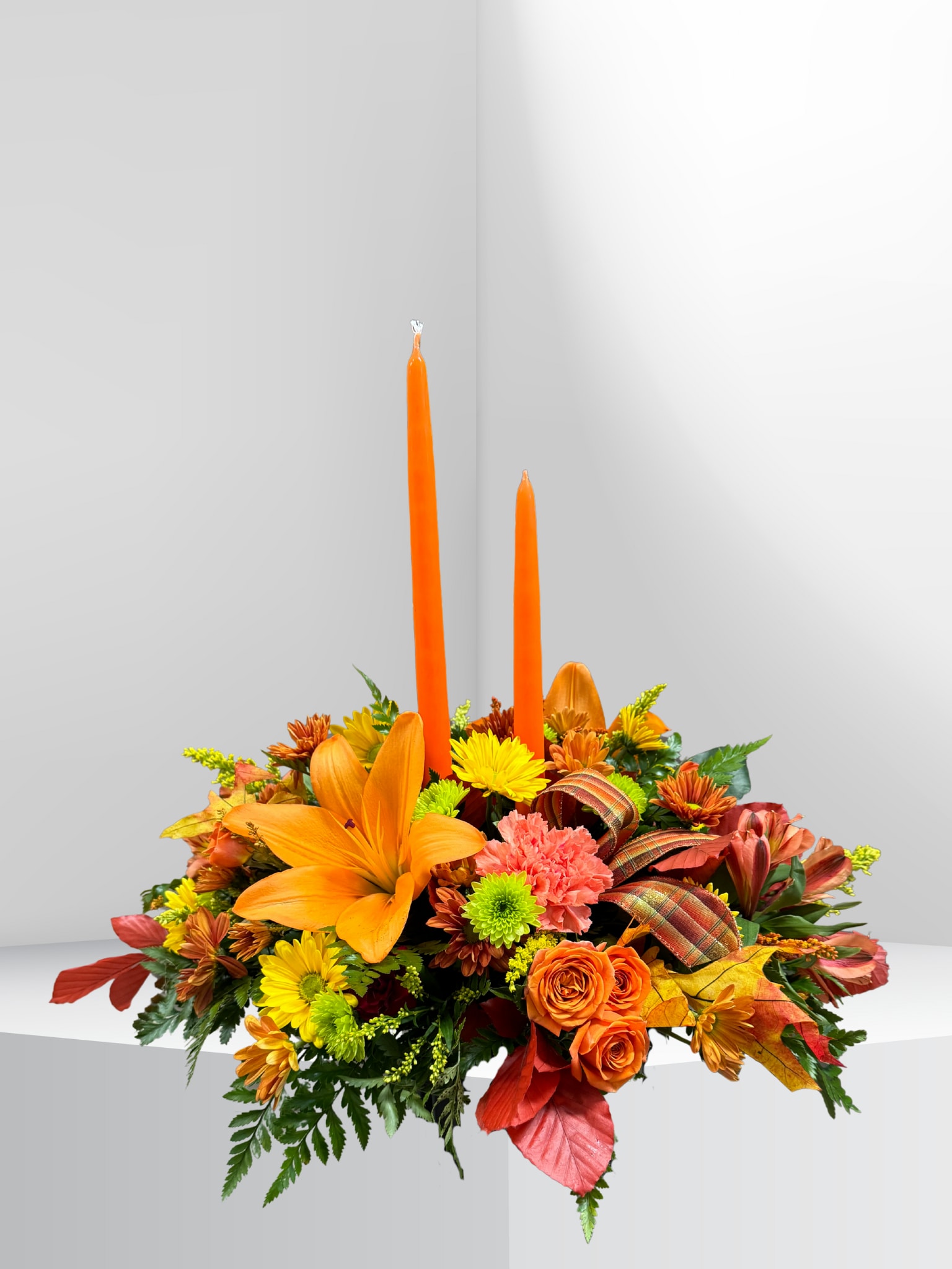 Thankful Traditions - Celebrate the beauty of the season with our Thankful Traditions centerpiece. Filled with a vibrant mix of autumn colors, this festive arrangement accented with a charming bow and taper candles to create a warm, inviting glow. It’s a lovely addition to your Thanksgiving table and a beautiful way to share the spirit of the holiday.   Please note: Candle colors may vary based on availability