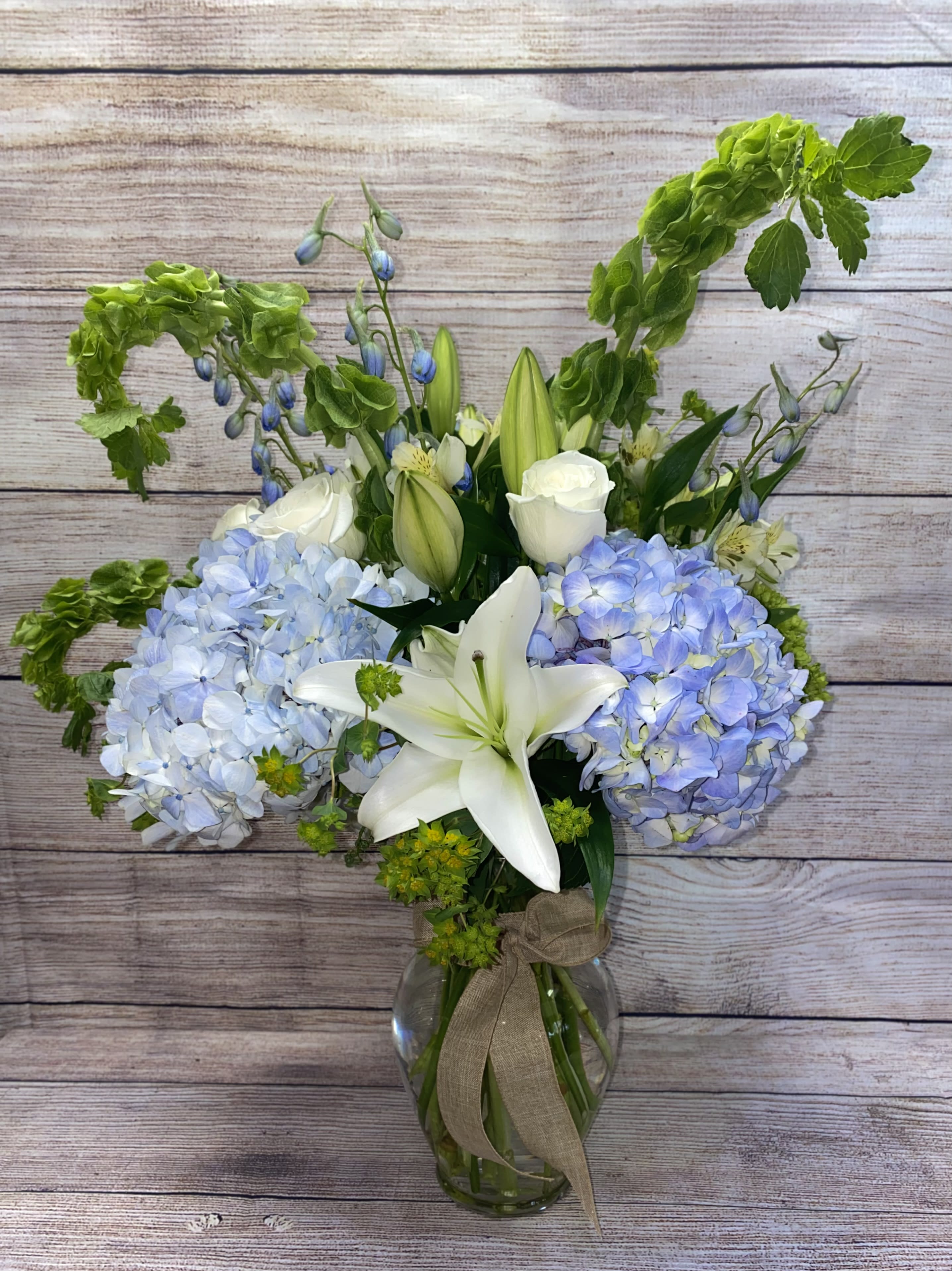 Breeze by the Sea  - This arrangement contains delphinium, bells of Ireland, lilies, hydrangea, roses and other seasonal blooms in shades of blues and whites. It is a great gift for a birthday, get well, for wishing someone a fresh start.
