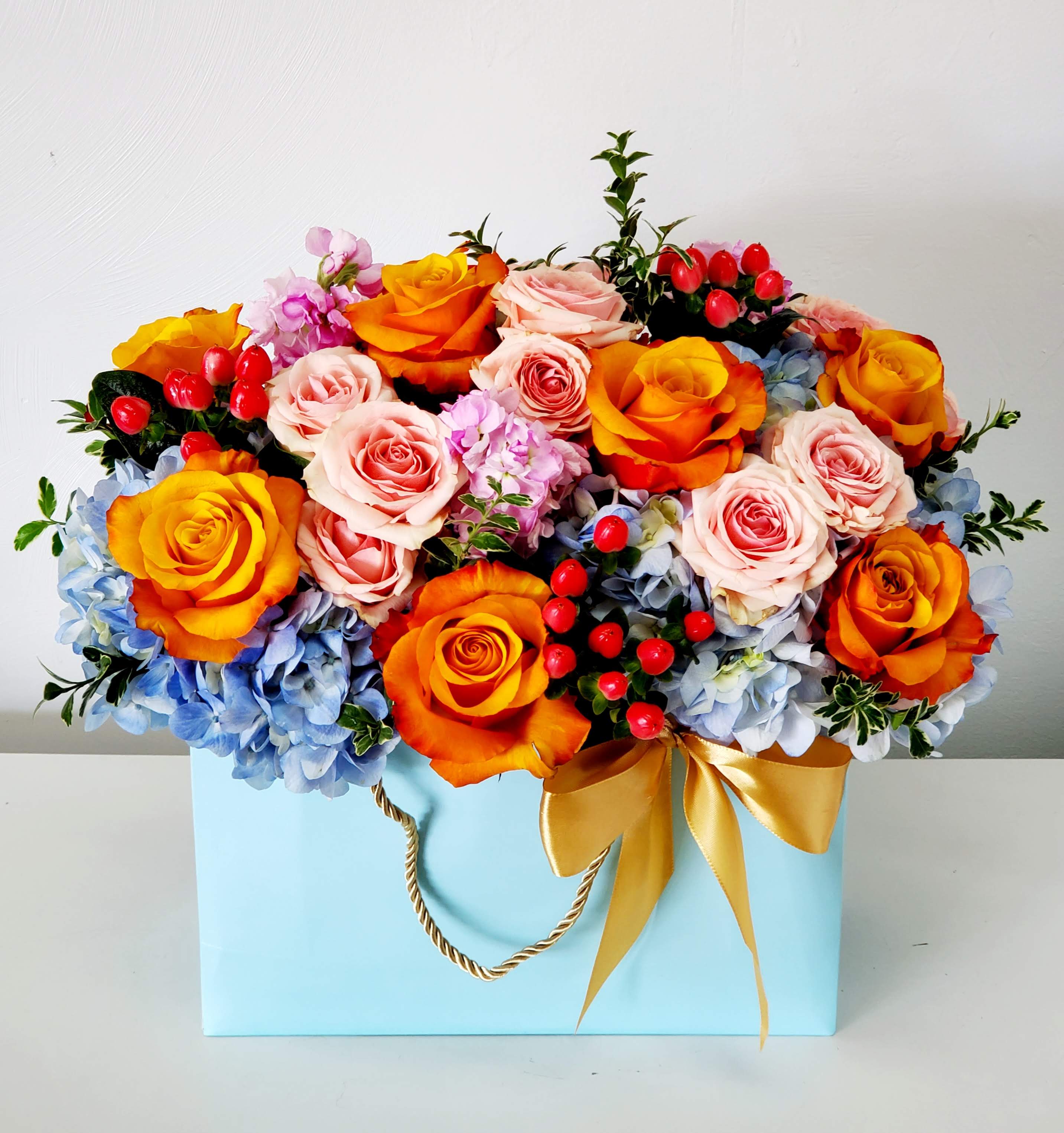Horizon - Meet Horizon—where blue skies meet golden sunsets in one gorgeous bouquet! Picture dreamy blue hydrangea paired with bold orange roses that practically glow, all softened by charming light pink spray roses. Designed in a blue bag, this cheerful blend is ready to brighten someone's day and spark joy wherever it lands. Perfect for adding a pop of color and personality to any space.  AS SHOWN: PREMIUM  0NE SIZE ONLY 15&quot; Wide by 13&quot; Tall