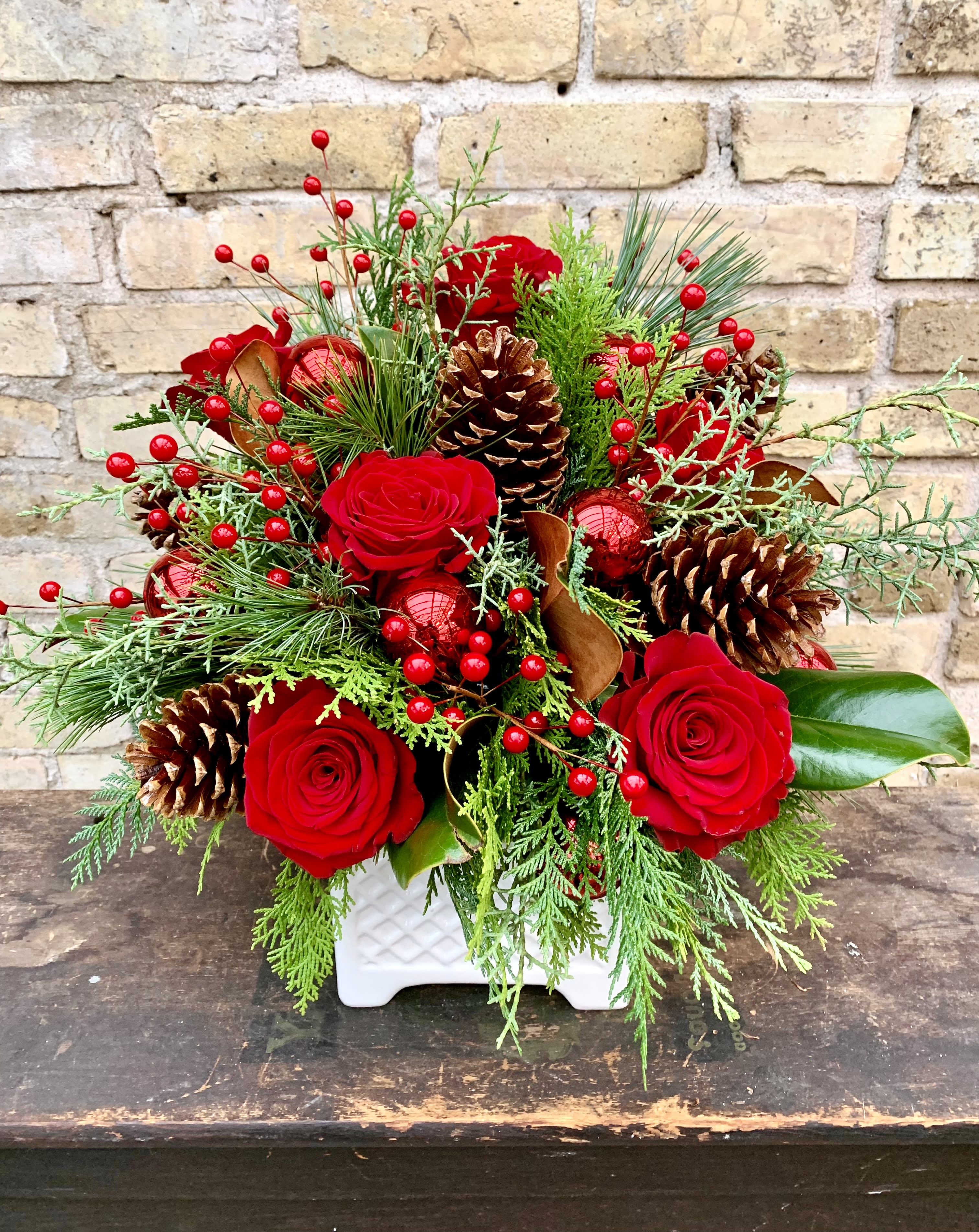 Dasher - Beautiful Assortment of Winter Greens, Red Berries,  Pine Cones Red Roses and Holiday Bling.  Designed in a White Ceramic Container. 