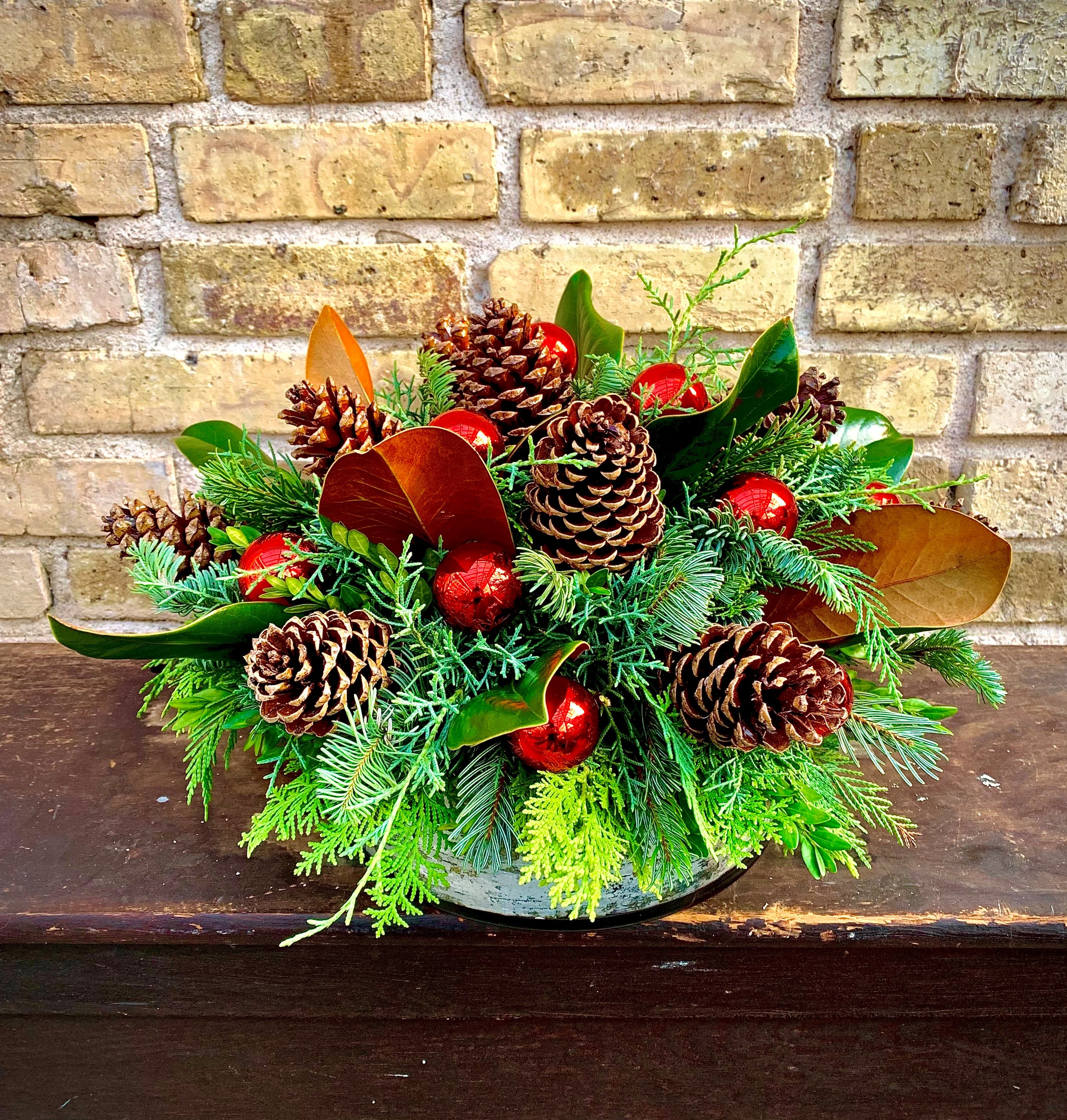 Forest Elegance - A Beautiful Assortment of Evergreens, Pine Cones, Magnolia and Millimeter Balls Designed in a Low Glass Container With Birch Ribbon Wrap. Simply Elegant.  Approximately 16&quot; wide x 8&quot;  Tall