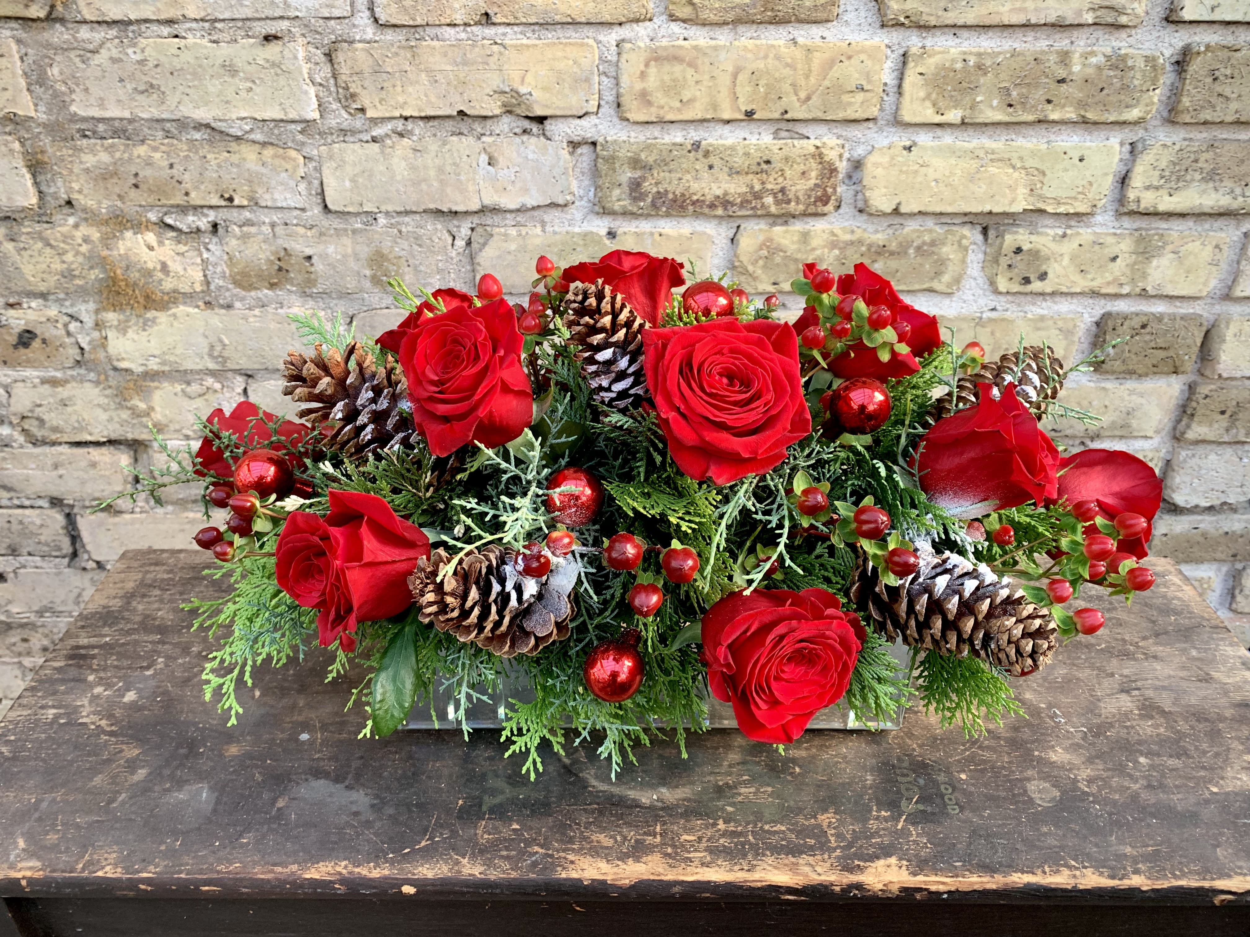Noel - Lush Holiday Arrangement With Pine Cones, Roses, Hypericum  and Winter Greens. This is Designed in a Rectangle Mirrored Container. A Great Centerpiece for Your Dining Table.