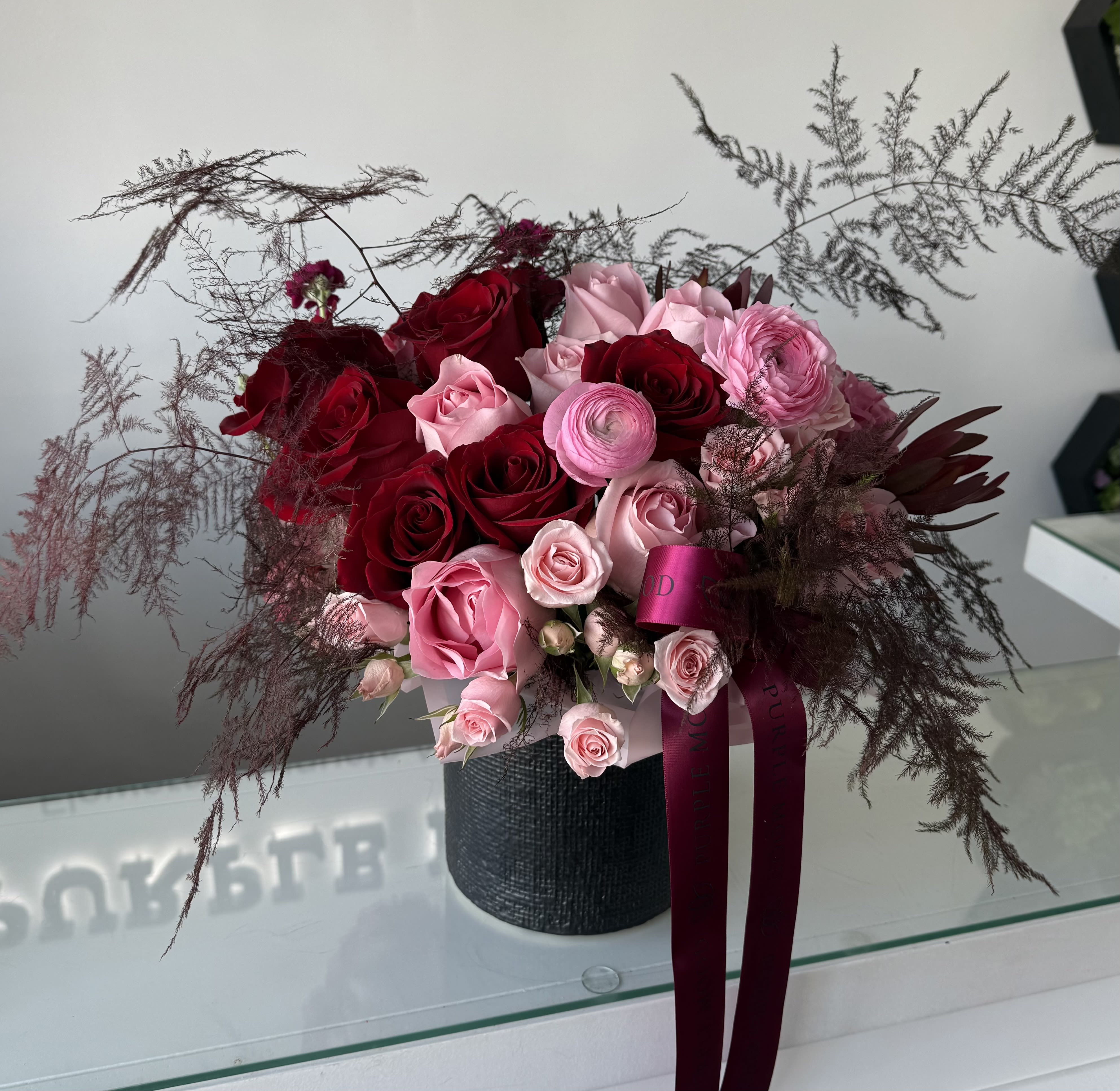 Love Me Vase - “Love Me Vase” is a stunning floral arrangement featuring an enchanting blend of premium red and pink roses, complemented by delicate ranunculus and soft foliage. Set in an elegant textured vase, it exudes sophistication and romance, making it the perfect gift for special occasions or simply to express love.