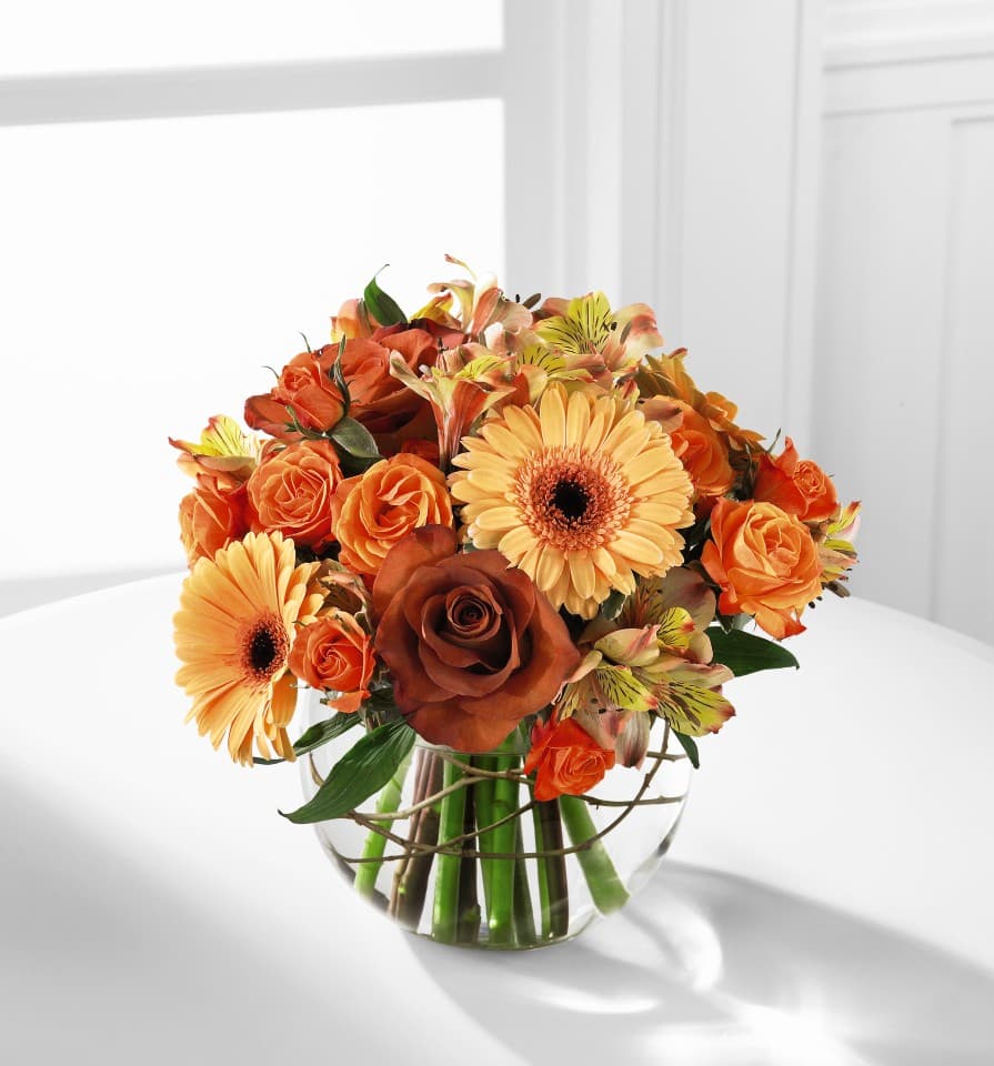 The FTD Natural Elegance Bouquet - The FTD Natural Elegance Bouquet ushers in the beauty and bounty of the Autumn season with abundant color mimicking the grandeur of this special time of year.  Lush Leonidas Roses, orange spray roses, golden gerbera daisies, and peach Peruvian Lilies are perfectly arranged in a clear glass bubble bowl vase to create a striking sentiment of gratitude and warmth.