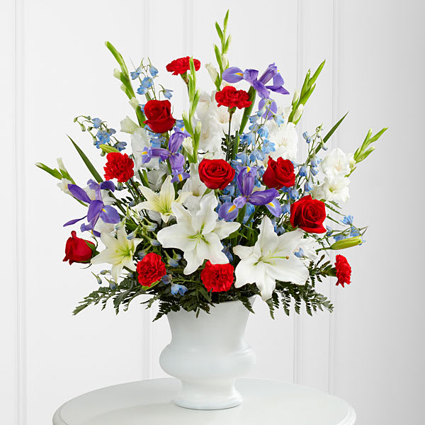 The Cherished Farewell Arrangement - The Cherished Farewell Arrangement is an elegant display of patriotic beauty to honor your loved one at their final farewell service. Red roses red carnations white gladiolus light blue delphinium blue iris white Oriental lilies white Asiatic lilies and lush greens are elegantly arranged in a white plastic urn to create a stunning way to say your last goodbye.