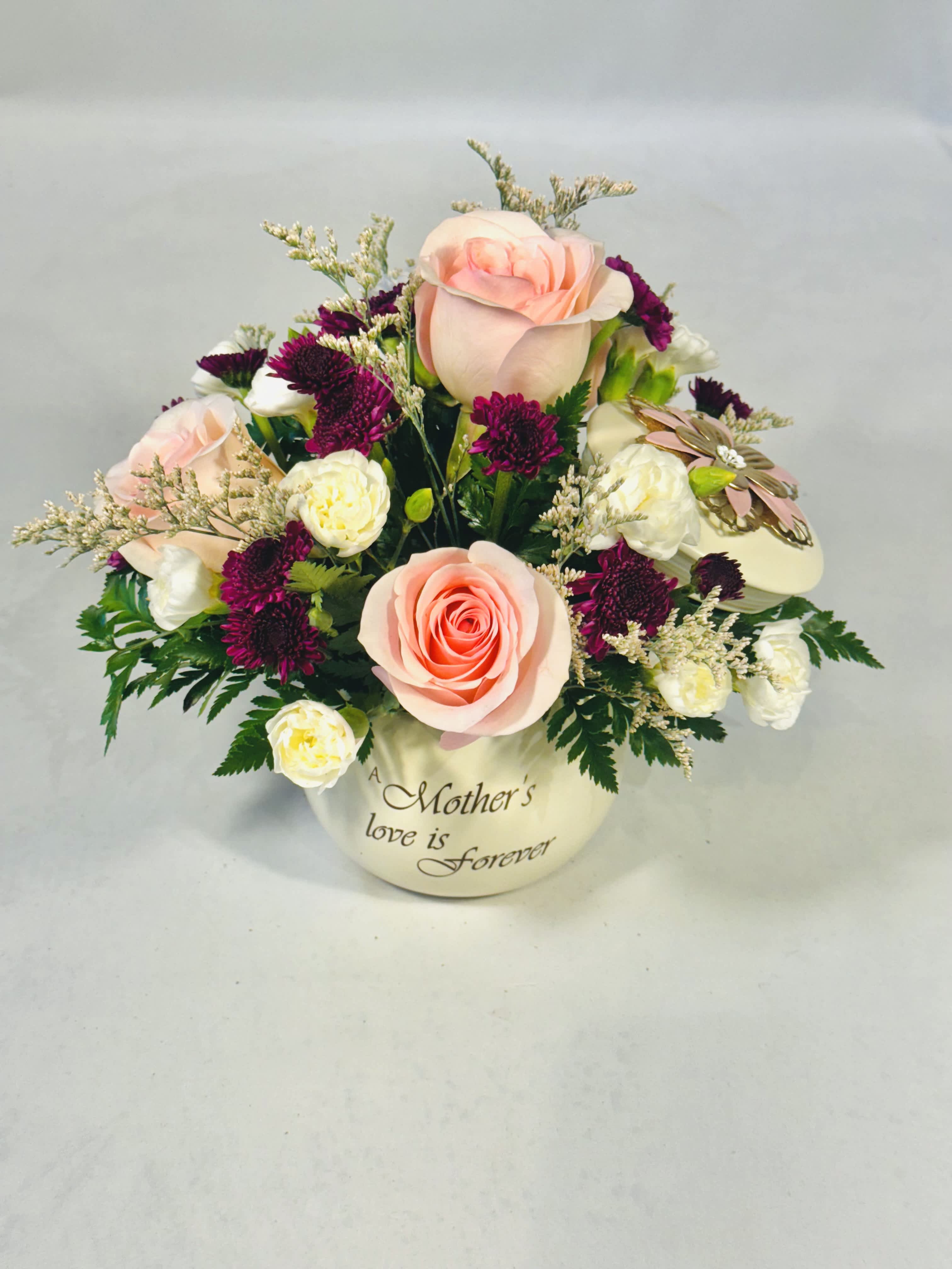 &quot; A Mother's Love&quot;  -  “A Mother’s Love is Forever.” This beautiful keepsake can later be used as a jewelry or trinket box for an everlasting reminder of how much love you have for your mom. Adorned with pink roses, purple buttons, mini white carnations and limonium with lush greenery.  Standard 9&quot;x 9&quot; Deluxe   12&quot;X 12&quot;