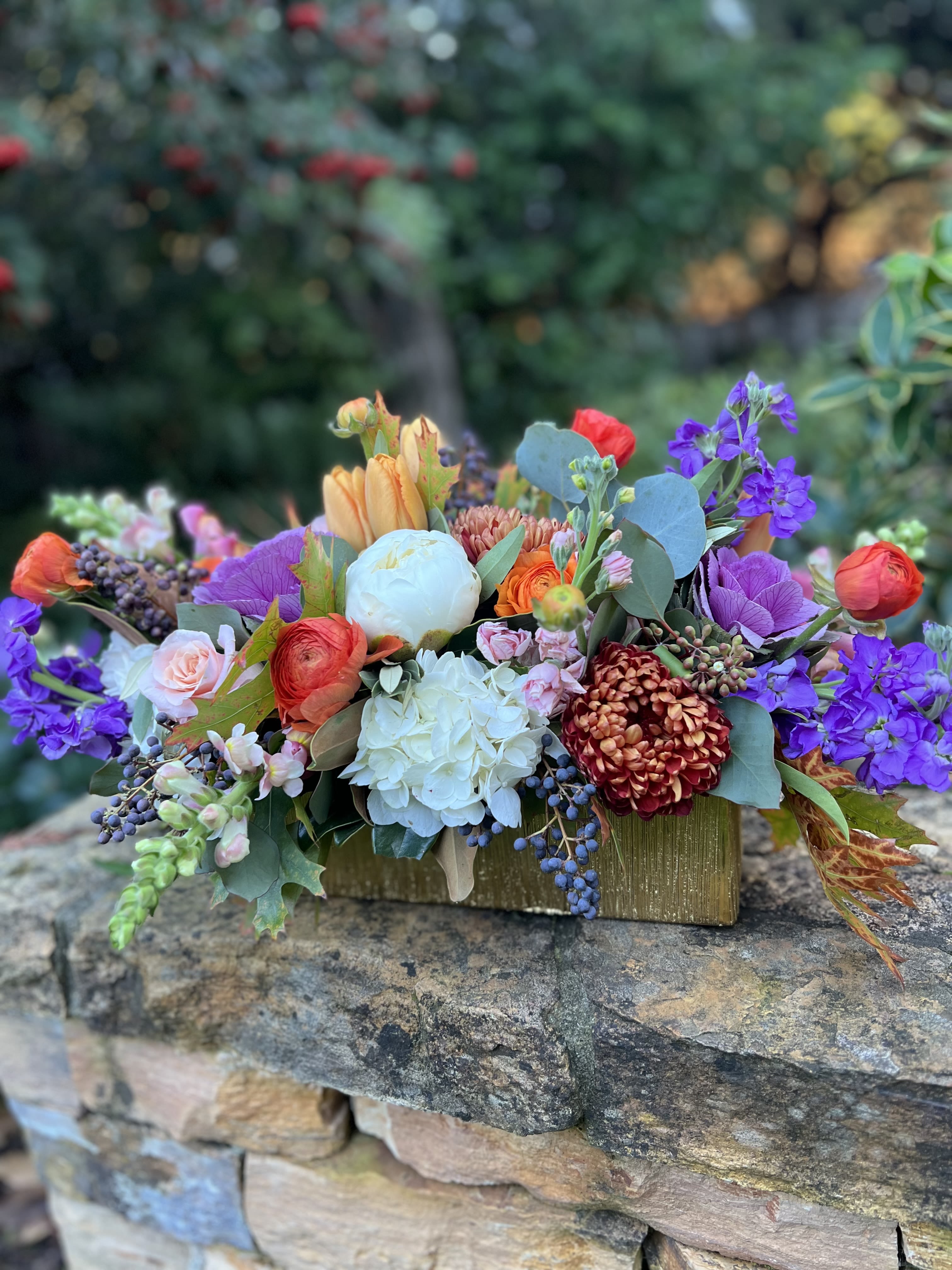 Giving Thanks - A long and low beauty arranged in a gold rectangular container filled with purple cabbage, stock, white peonies, seasonal mums, hydrangeas, ranunculus, roses, oak leaves and privet berries; the table is set! 