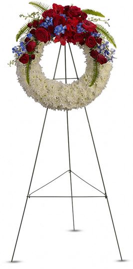 Serenity Wreath Standing Spray Arrangement  - A circle of remembrance shows through this beautifully designed wreath. Covered with white button mums. The top of the arch is decorated with roses, ferns, &amp; accented blue delphiniums. If you would like a ribbon with wording, i.e.. Mother, Father In-Law, Beloved Cousin, etc. Please contact us for additional pricing.