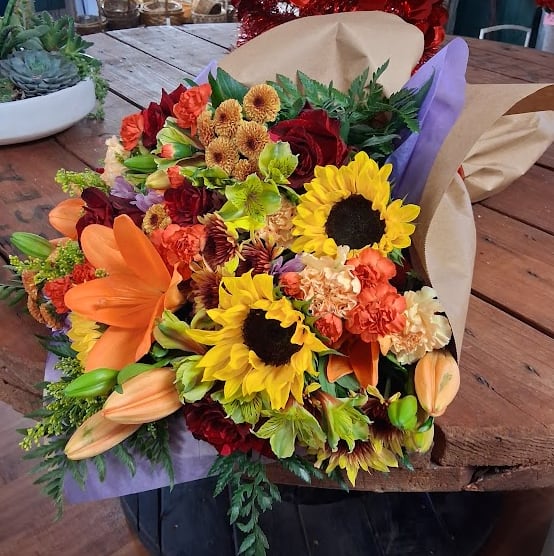 Grand Fall Bounty Bouquet - Brimming with the rich beauty of the season, this large bouquet is a gorgeous gathering of assorted fall blooms in their most vibrant moment. Lush mums, radiant roses, golden sunflowers, rustic daisies, and wisps of seasonal foliage come together to create a full, textured display bursting with warmth. Perfect for gifting, celebrating, or brightening any space “just because,” this generous bouquet brings the cozy charm of autumn right into your arms.