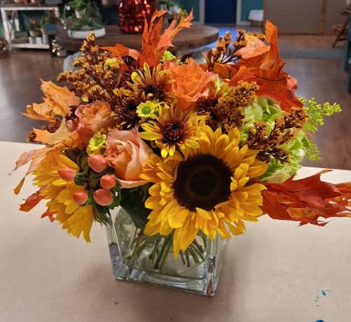 Rustic Sunshine - Awaken any space with the warm glow of Rustic Sunrise, a grand seasonal arrangement designed in an elegant square vase. This generously sized bouquet blends rich fall blooms in shades of amber, cranberry, gold, and soft sunrise peach. Lush roses, mums, rustic daisies, and textural accents spill upward and outward, creating a radiant display that feels both refined and earthy.  Perfect for making a statement on a dining table, entryway, or as a luxurious gift, Rustic Sunrise captures the quiet beauty of an autumn morning — warm, glowing, and full of promise.