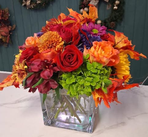 Fluorescent Fall - Bring pure joy and energy into any room with Autumn Colorburst, a lively and abundant arrangement designed in a large, elegant square vase. This bouquet is a celebration of color — bursting with rich reds, sunny yellows, vivid oranges, bold purples, and pops of playful pink. A cheerful mix of seasonal blooms like roses, mums, asters, carnations, and daisies come together in a bright, eye-catching display that feels fun, festive, and full of life. Perfect for anyone who loves bold color and big smiles, turn any moment into a celebration of fall’s most brilliant hues.