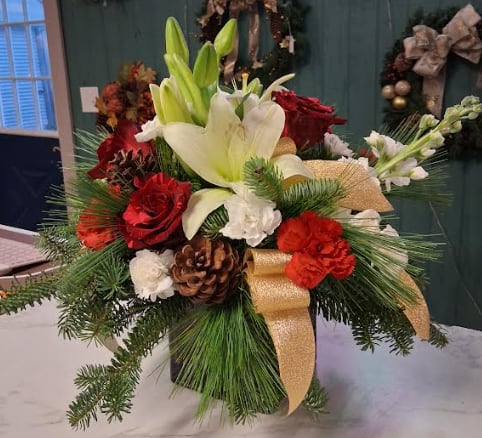 Family Tradition - Designed in a striking red cube, this sophisticated Christmas arrangement brings timeless holiday beauty to any home or gathering. Lush seasonal evergreens set the stage for classic Christmas blooms—rich red roses, festive carnations, snowy white accents, and delicate seasonal fillers. Finished with subtle holiday textures and graceful touches, Family Tradition captures the warmth, charm, and magic of the season in a refined, modern display.  Let me know if you’d like a more whimsical version, a larger upgrade description, or one with sparkle!