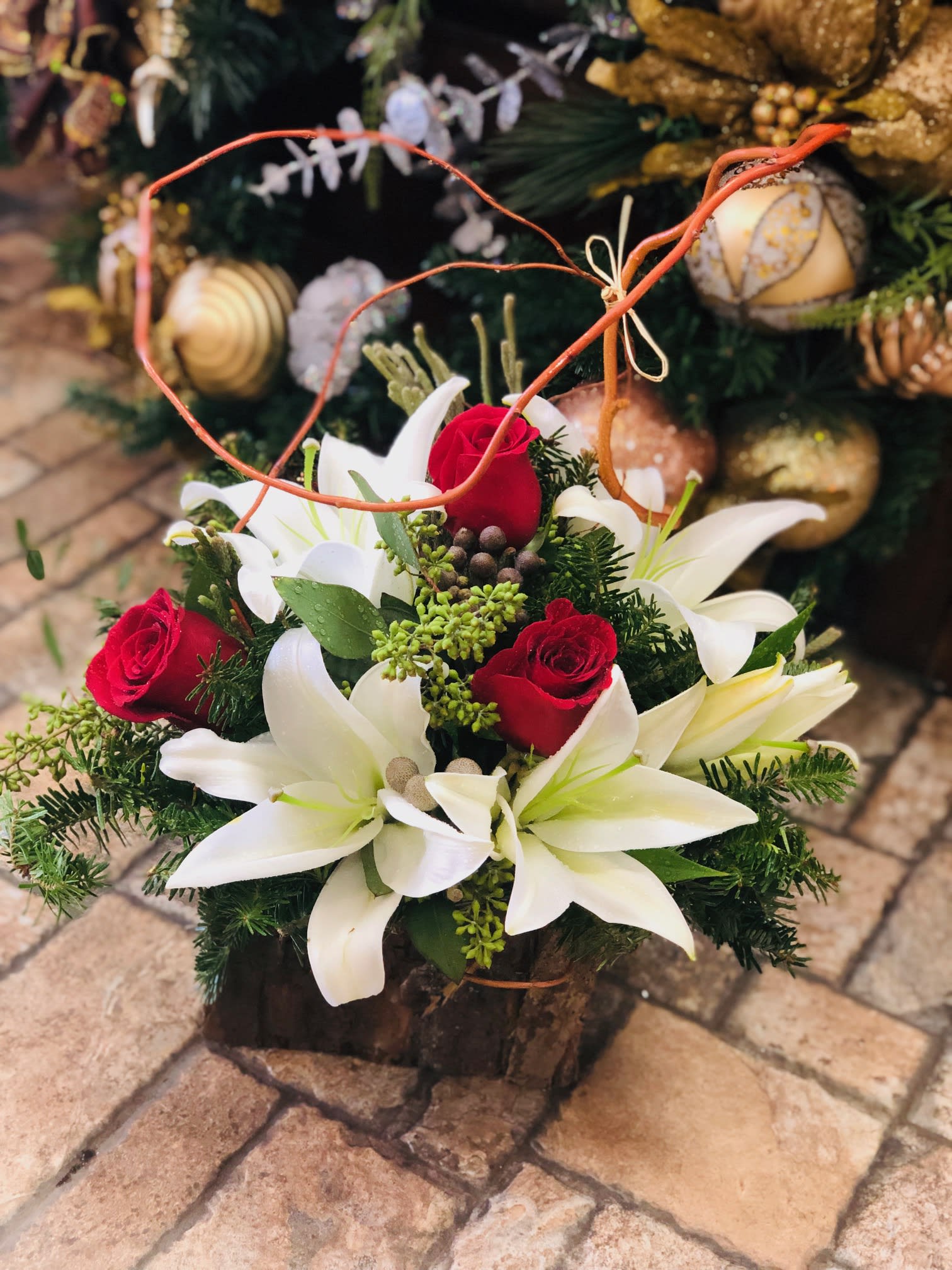 Christmas Box - Celebrate the beauty of the season with this stunning Christmas arrangement featuring radiant white lilies and rich, velvety red roses. The crisp white petals symbolize peace and purity, while the deep red roses add timeless warmth and romance. Nestled among fresh evergreens and accented with festive holiday touches—such as pinecones, ornaments, or subtle ribbon detailing—this arrangement brings classic Christmas elegance to any space. Perfect as a centerpiece, gift, or holiday décor accent, this design blends sophistication with seasonal charm, creating a breathtaking display that captures the true spirit of the holidays.