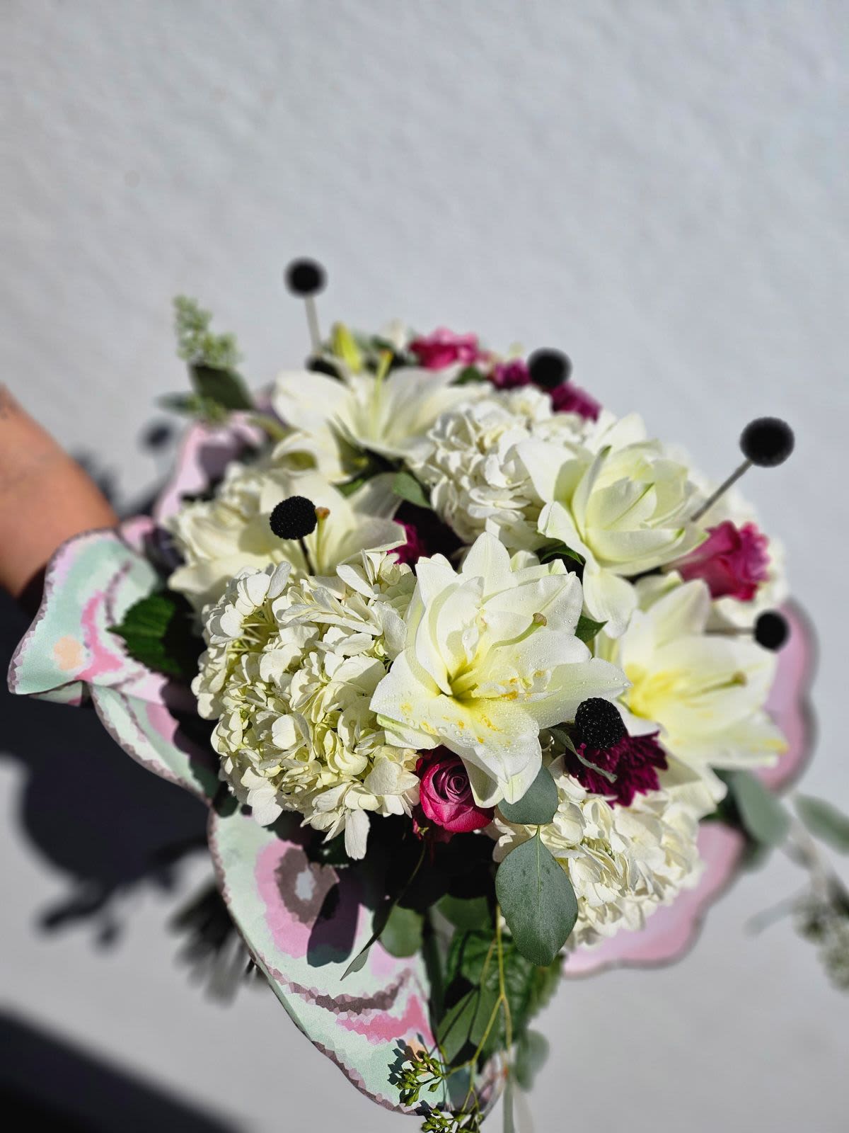 Blooming Butterfly - A premium wrapped bouquet with a mixed variety of flowers including lilies and hydrangea. A touch of pink and black makes this bouquet elegant and classy like a beautiful butterfly. Flowers may vary, vase not included. 