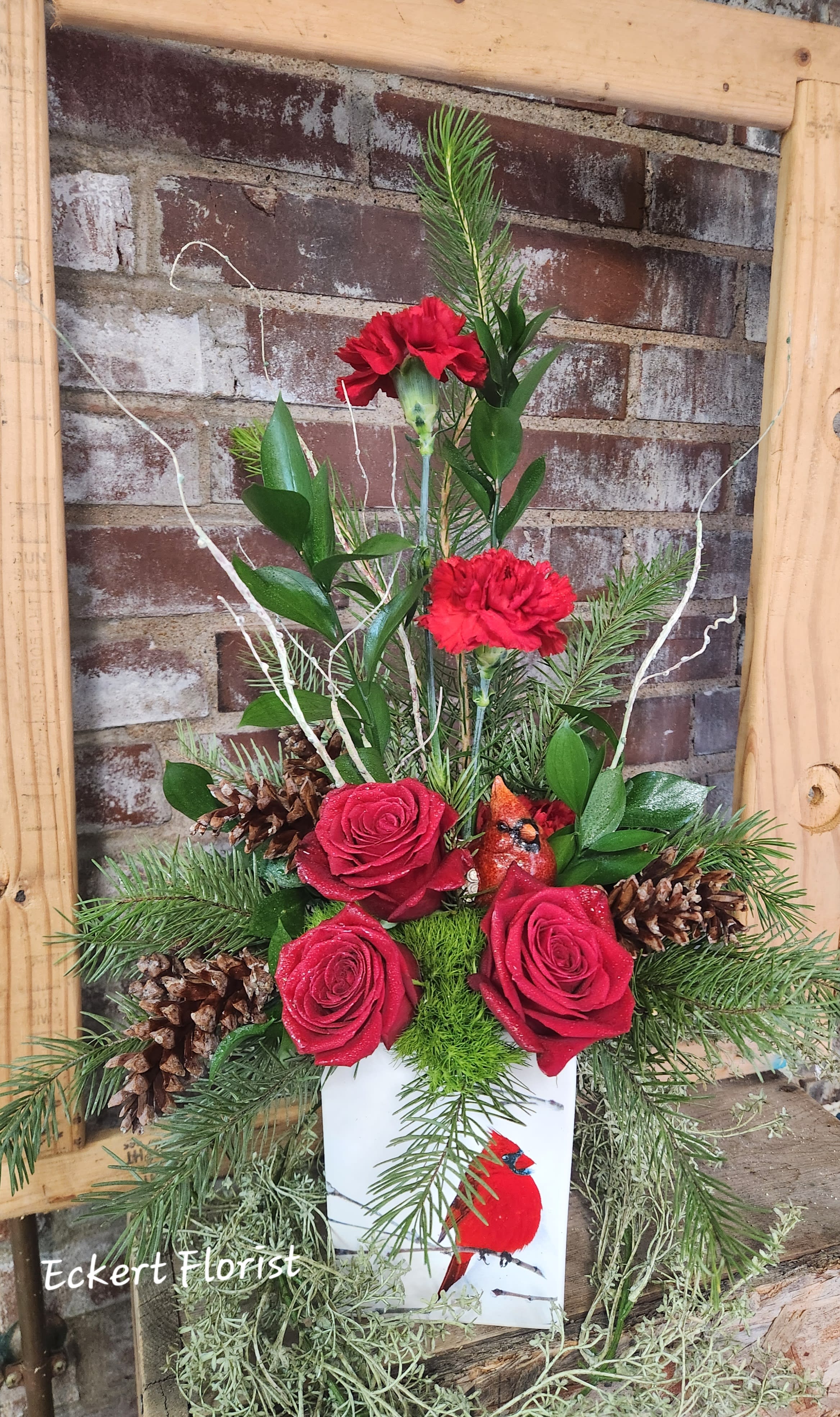 Eckert Florist's Cardinal Winter Arrangement *LOCAL DELIVERY ONLY - Made in a white ceramic container with a white birch and cardinal bird motif, this fresh holiday arrangement features a ceramic keepsake cardinal bird surrounded by carnations, roses, pine cones and winter greens. *LOCAL DELIVERY ONLY