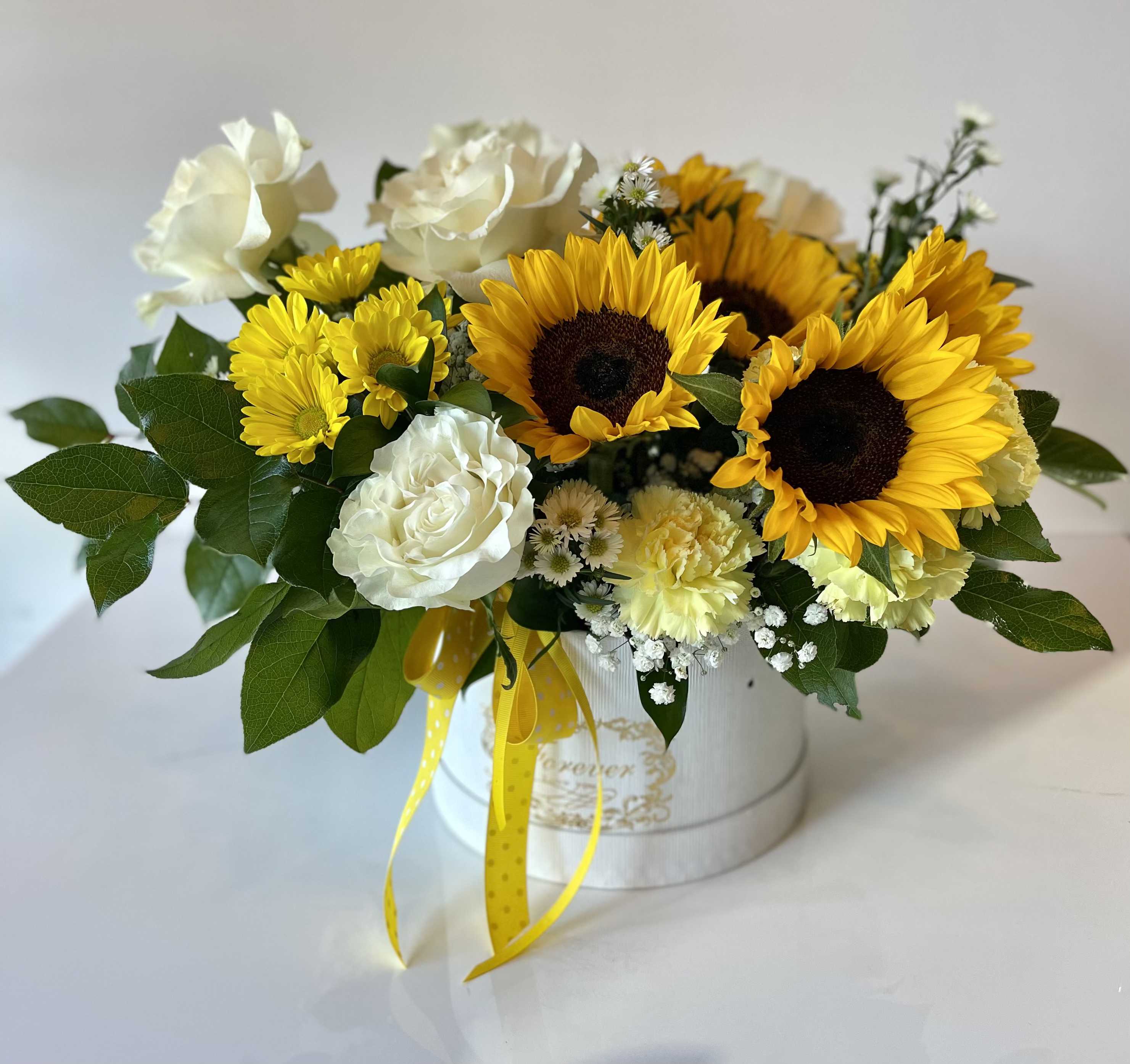 Golden Sunshine Box - Bring a burst of happiness into any space with our Golden Sunshine Box! This radiant arrangement features bold, golden sunflowers, creamy white roses, cheerful yellow chrysanthemums, and soft yellow carnations—accented with delicate daisy-like asters and lush greenery. Designed in a chic box with a matching yellow ribbon, it’s a joyful and uplifting gift for any occasion.  Perfect for birthdays, congratulations, or simply to brighten someone’s day, this vibrant bouquet is sunshine in floral form.
