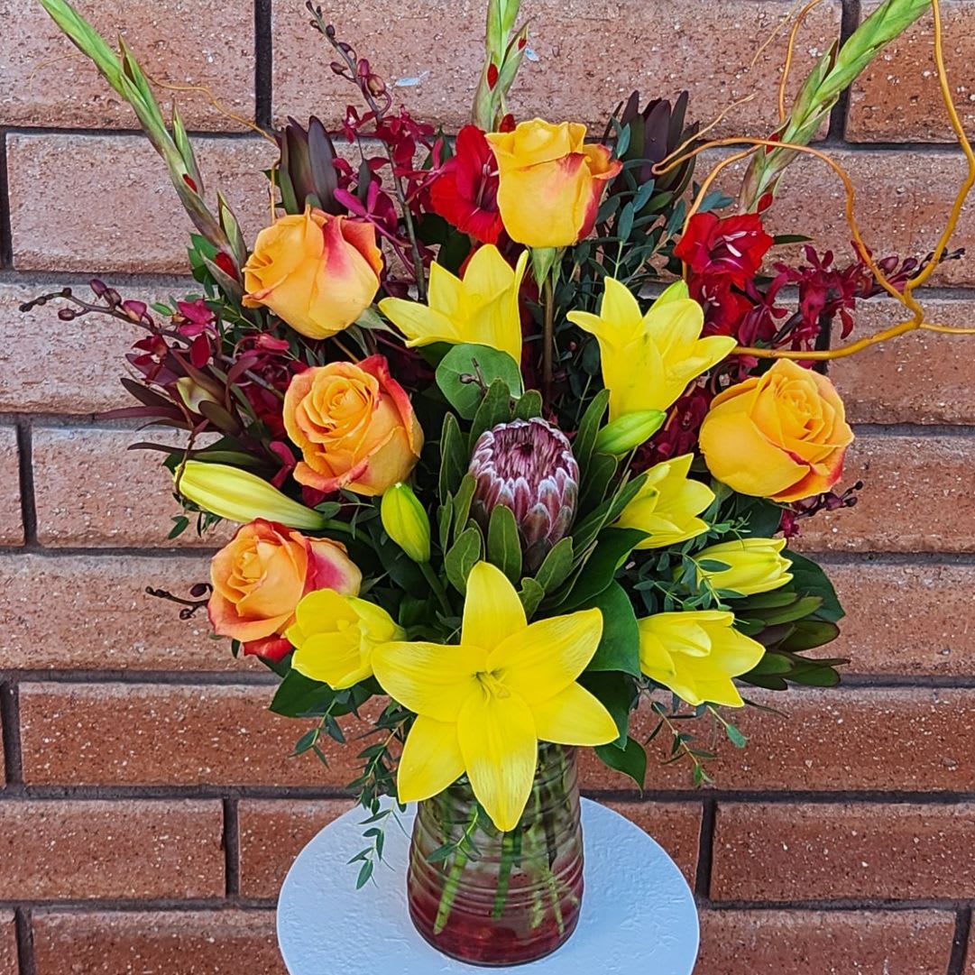 The Firecracker Bouquet - The Firecracker Bouquet – Exotic Orchids, Proteas, Lilies &amp; Roses  Turn up the heat with our Firecracker Bouquet, a stunning mix of exotic blooms and bold textures designed for those who love flowers that make a statement. This vibrant, year-round favorite features Red Elephant Orchids, Proteas, Lilies, Roses, and Gladiolus, all beautifully hand-arranged in a premium clear glass vase.  Unlike traditional autumn arrangements, Fiery Elegance offers a modern, tropical-inspired look with its warm color palette and sculptural design. Whether sent as a gift or displayed as a centerpiece, it’s sure to leave a lasting impression.  Available Sizes:  • Standard (One-Sided Presentation) – 4 lilies, 3 gladiolus, 5 roses, 3 red elephant orchids, 4 safari sunset proteas, 1 pink ice protea, and fresh garden greens in a designer glass vase (approx. 18&quot; W x 29&quot; H)  • Deluxe (Full/Round Style Design) – 5 lilies, 3 gladiolus, 9 roses, 4 red elephant orchids, 5 safari sunset proteas, 2 pink ice proteas, and fresh garden greens in a designer glass vase  • Premium (Jumbo/Round Style Design) – 6 lilies, 4 gladiolus, 12 roses, 5 red elephant orchids, 6 safari sunset proteas, 3 pink ice proteas, and fresh garden greens in a designer glass vase  Please Note: Most lilies will arrive in bud form to ensure maximum freshness and longevity. Remove the stamens once the blooms open to enhance their lifespan and prevent pollen staining.