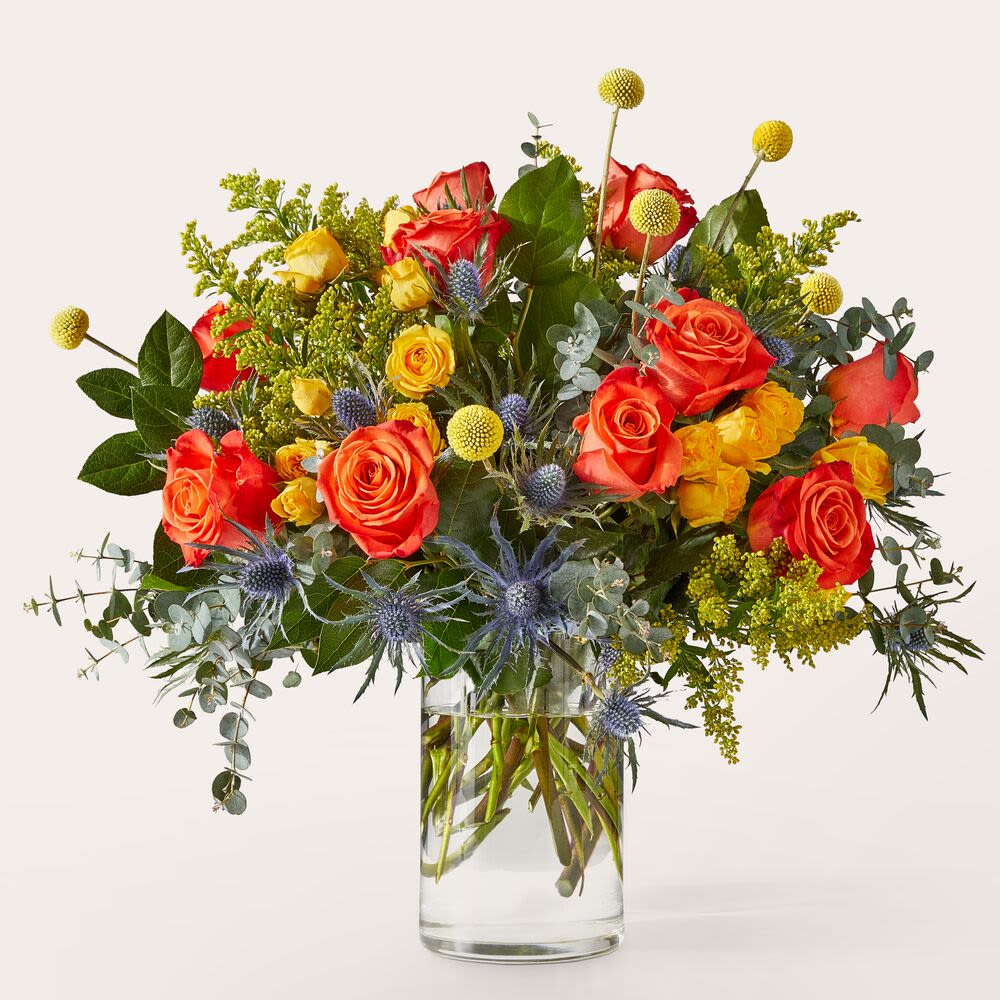 Miami Flowers Bouquet - Bring a bold and modern twist to floral gifting with this striking arrangement, expertly designed to stand out. Bursting with fiery orange roses, golden yellow spray roses, and cheerful billy balls, this bouquet radiates warmth and energy. Accented with textured blue thistle, lush greenery, and soft eucalyptus, the combination offers a rich and sophisticated look that's both contemporary and timeless. Presented in a clear glass cylinder vase, this arrangement is perfect for birthdays, congratulations, housewarmings, or sending a stylish &quot;just because&quot; surprise. The contrast of vivid warm tones with cool blue and silver elements adds depth and drama, making this bouquet a stunning centerpiece for any home or office. Freshly handcrafted by skilled florists, every stem is thoughtfully placed to create a visually captivating design. Order today for fast, reliable delivery and give the gift of color, texture, and modern floral beauty that’s sure to leave a lasting impression.