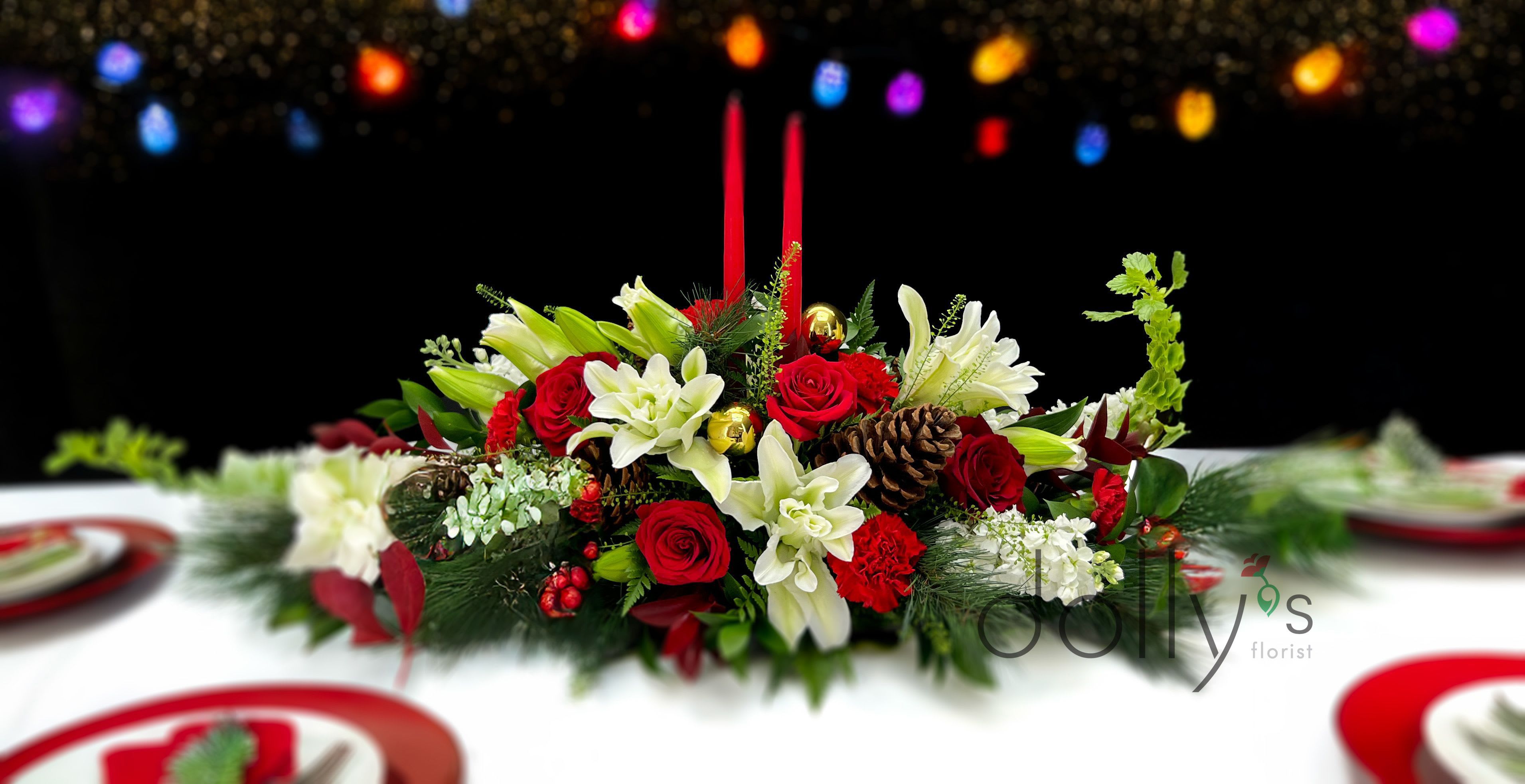 Centerpiece | Jolly - Celebrate the tradition with this elegant centerpiece, composed of roses, lilies, pine cones, adorned with 2 candles.