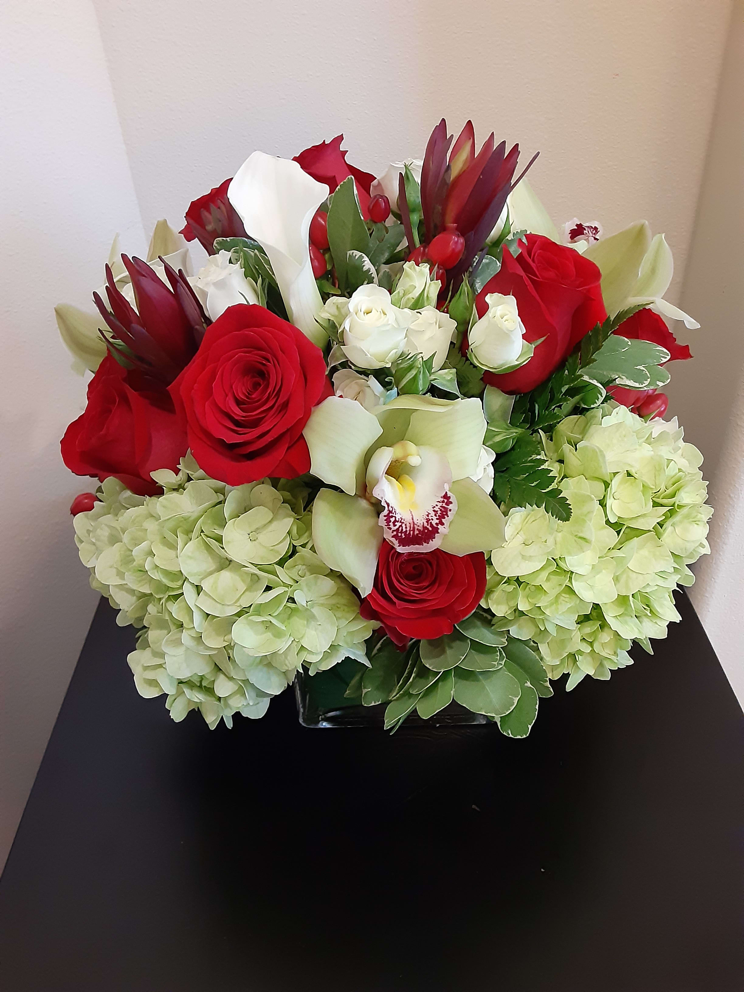 Ruby! - Red roses, white calla lilies, hydrangea, orchids in a contemporary modern square glass vase lined with a leaf.  