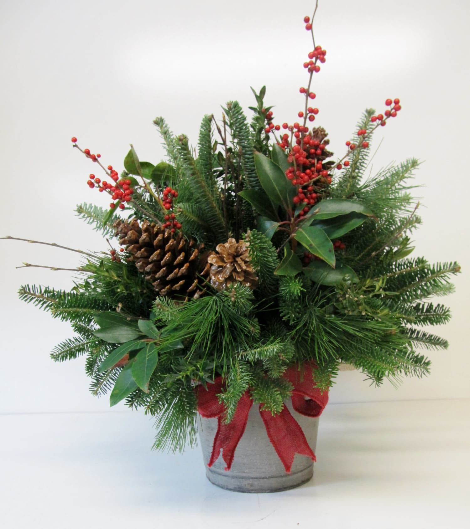 Christmas Berries and Greens - Floral arrangement with berries and winter greens assorted with ribbon in a country container-can add flowers if desired