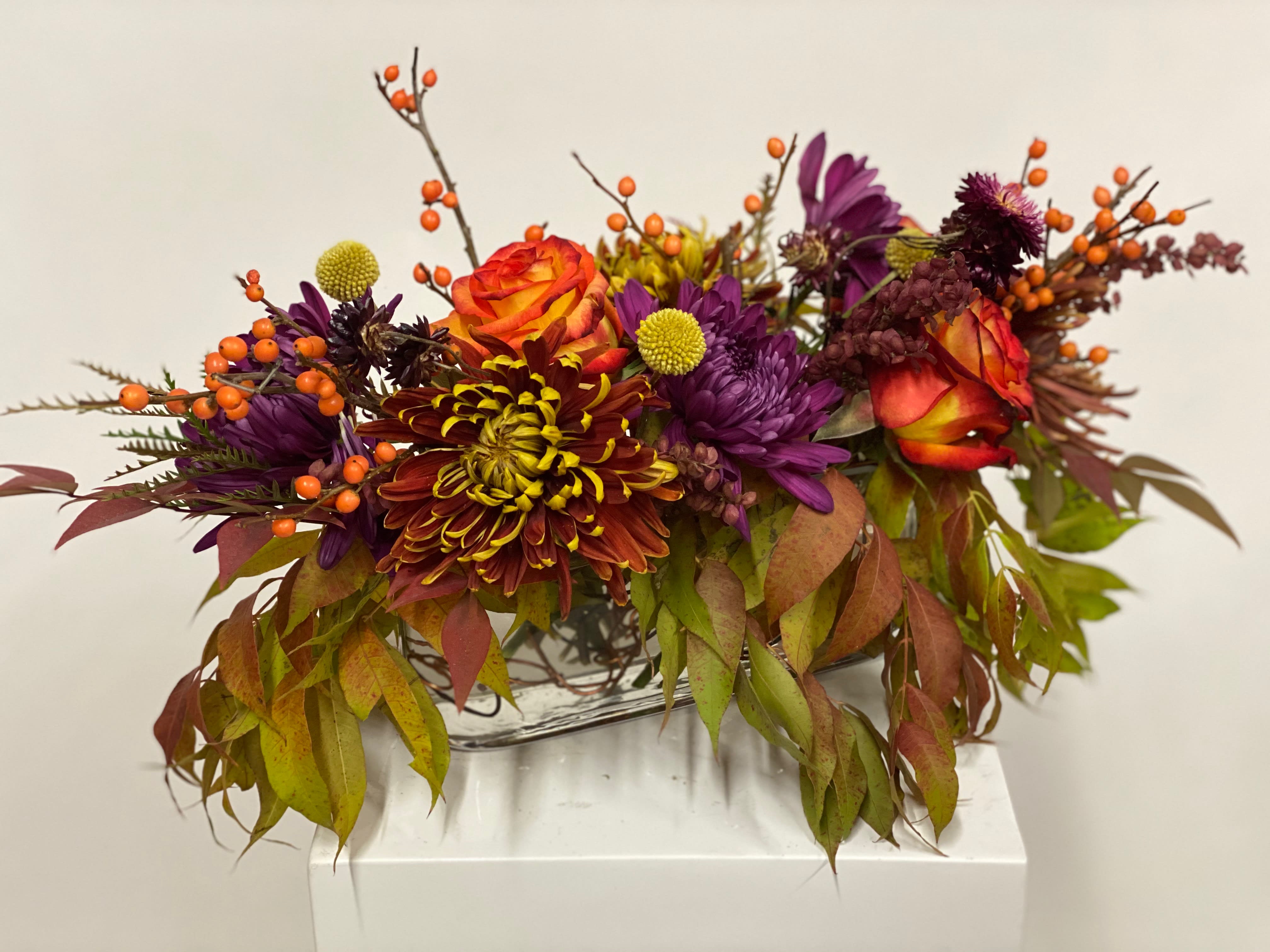 Feels like Fall - Fall inspired arrangement in 12 inch long vase with roses, mums and fall foliage.  Perfect hostess gift for the holidays.